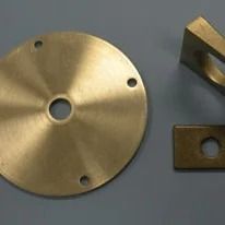 Three brass-colored metal components: a circular plate, a bracket, and a rectangular piece.