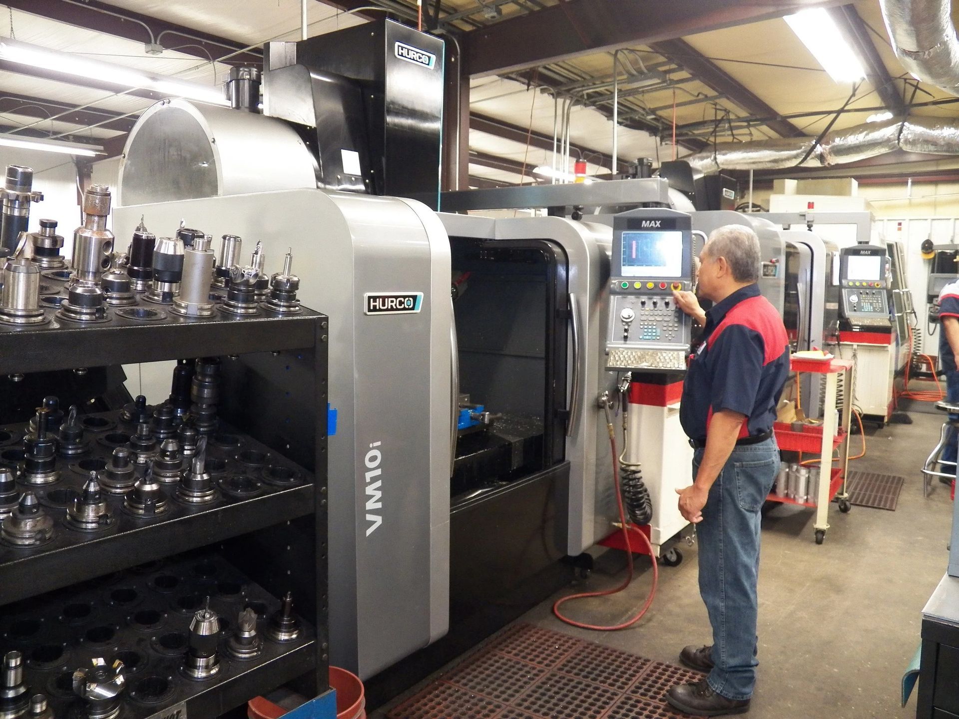 Man operating a CNC milling machine in a manufacturing facility. Machine is grey with a control panel.