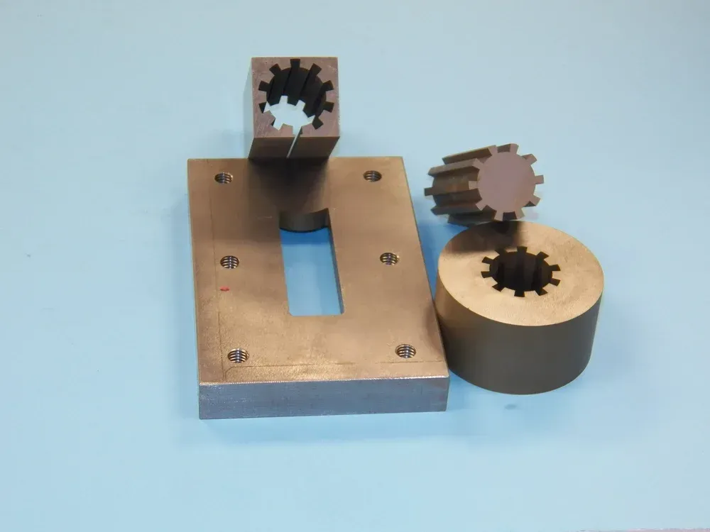 Metal mechanical parts on a blue surface, including a plate, square block, and toothed gears.