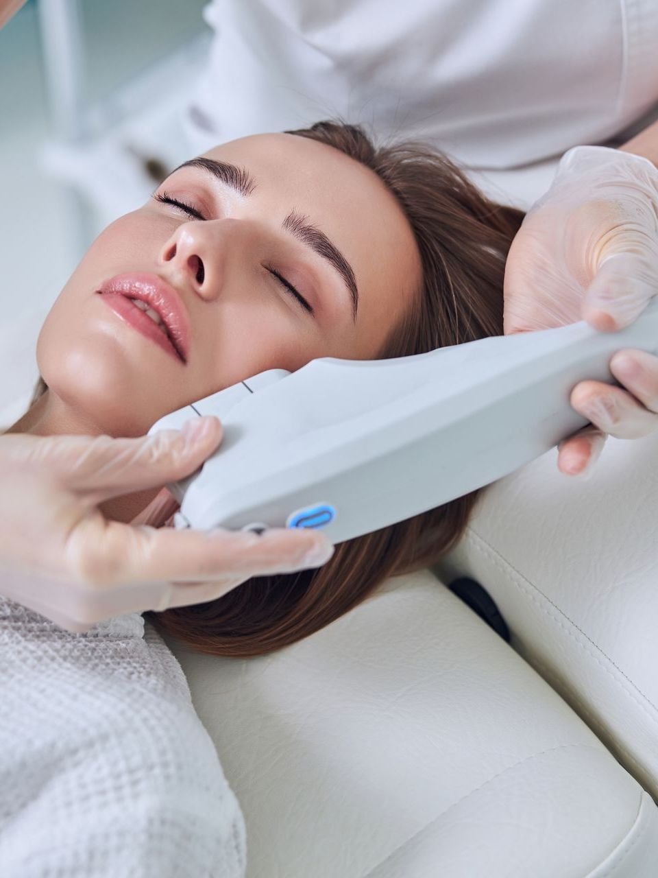 A woman with her eyes closed is getting a facial treatment