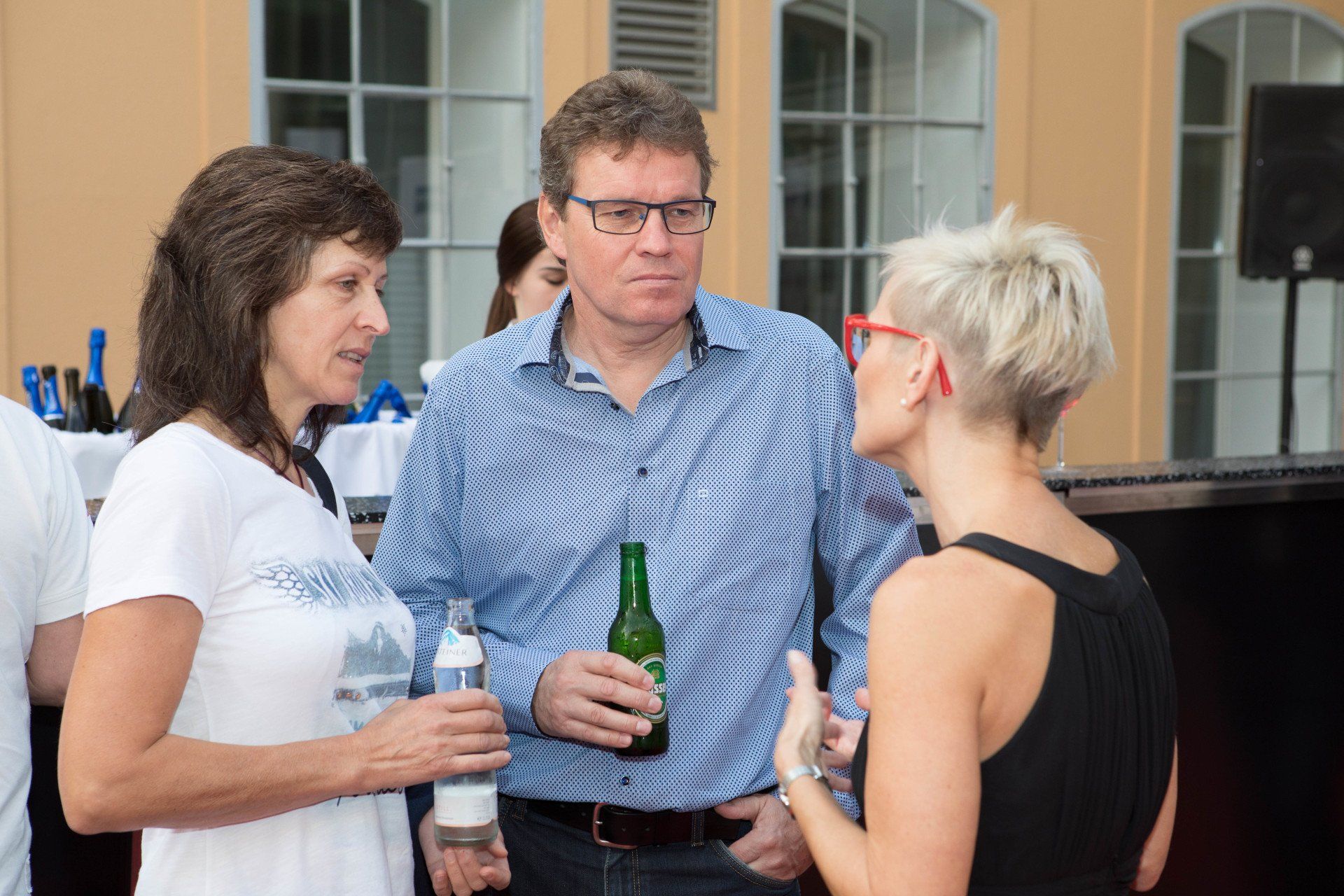 Ein Mann und zwei Frauen unterhalten sich, während sie Bierflaschen in den Händen halten.