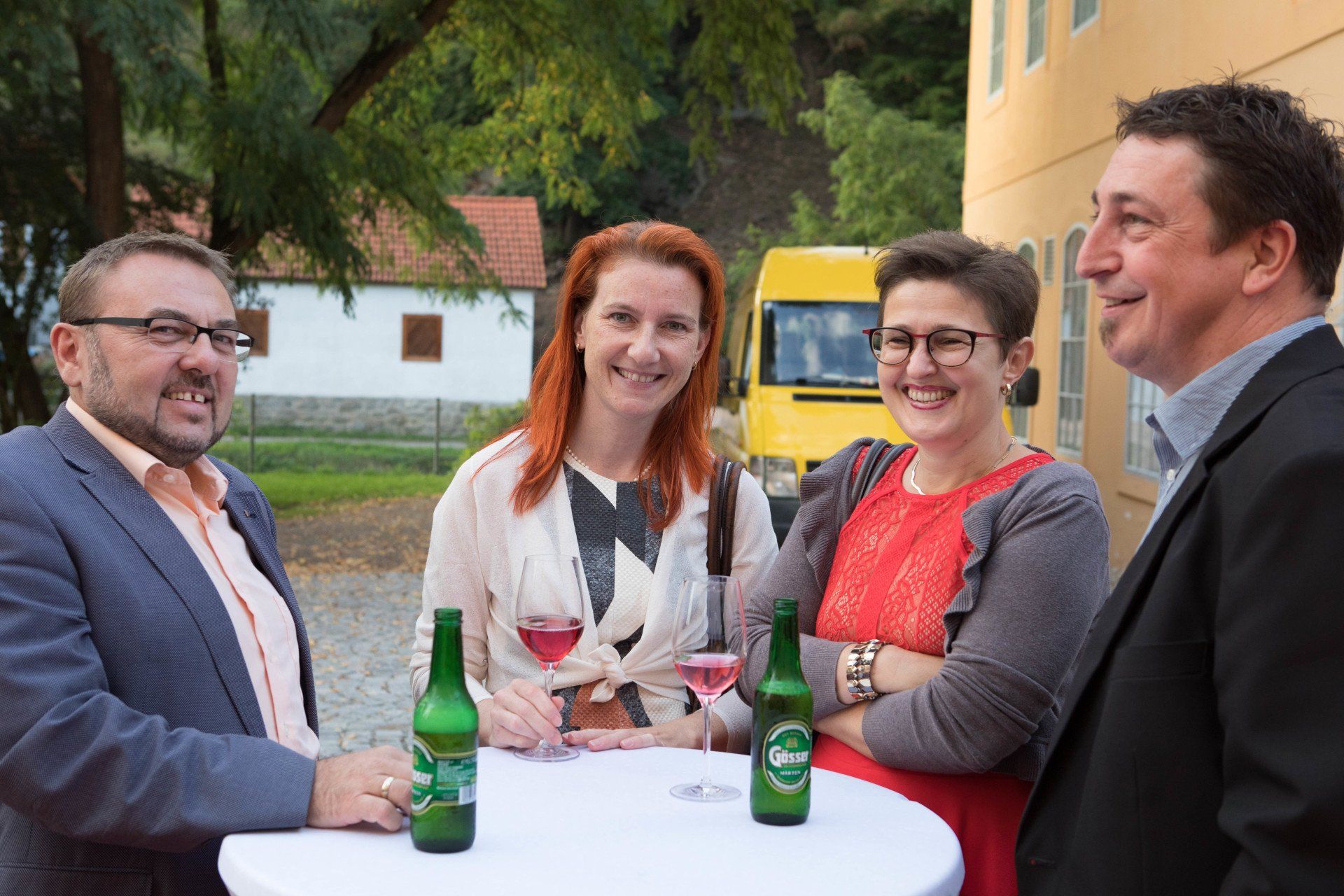 Eine Gruppe von Leuten sitzt mit Bier- und Weinflaschen um einen Tisch herum.
