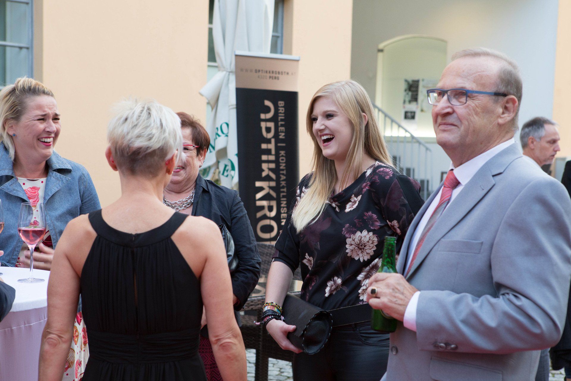 Eine Gruppe von Menschen steht vor einem Schild mit der Aufschrift „Optikkro“.