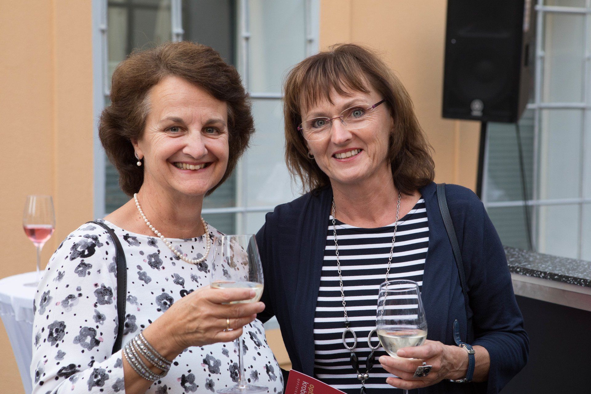 Zwei Frauen stehen nebeneinander und halten Gläser Wein in der Hand.