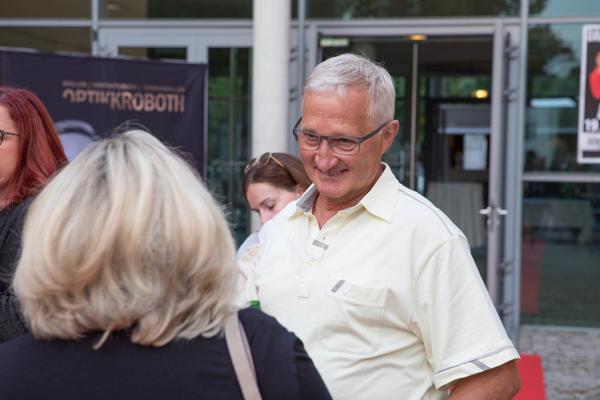 Ein Mann mit Brille spricht vor einem Gebäude mit einer Frau.