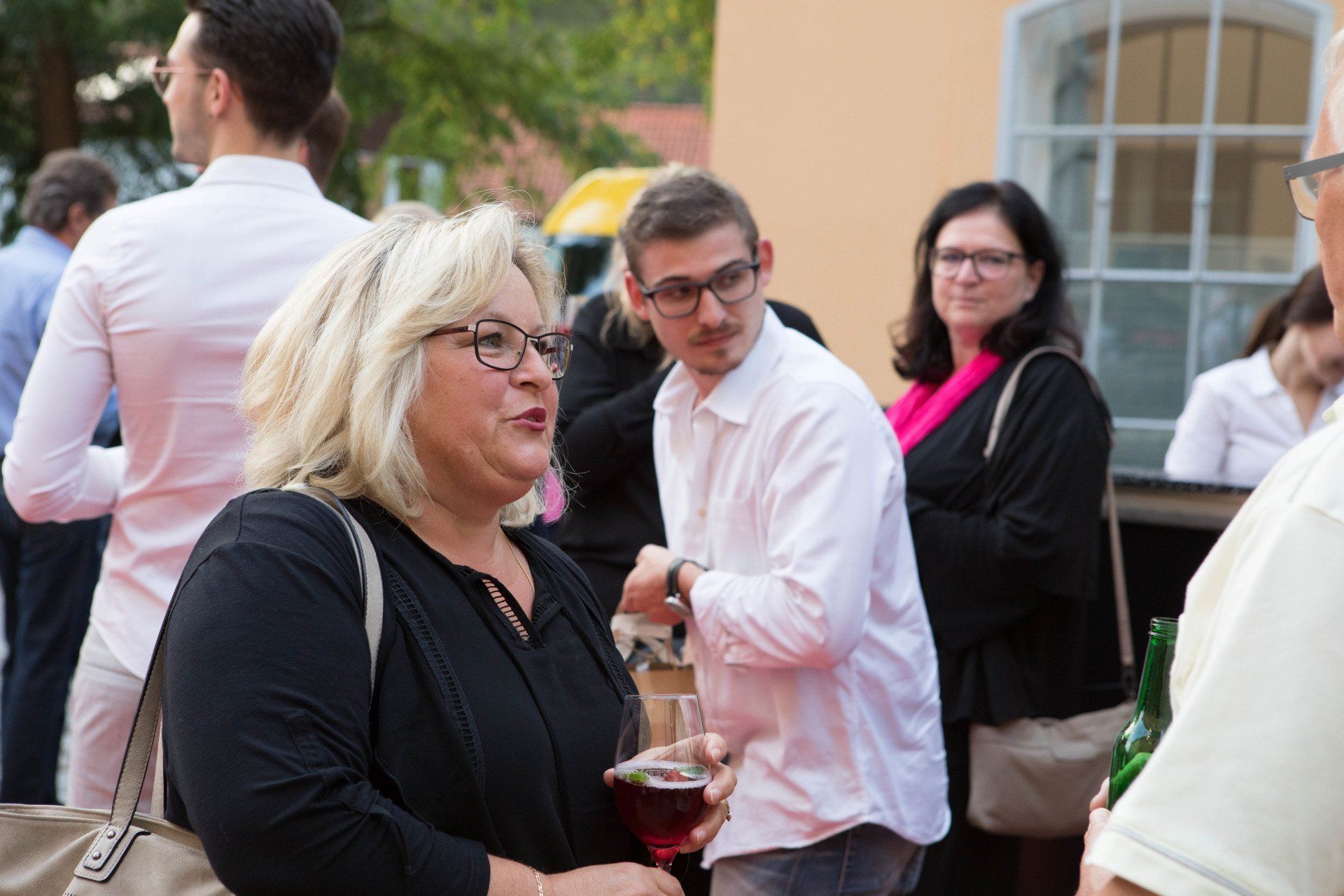 Eine Gruppe von Leuten steht herum, unterhält sich und trinkt Wein.