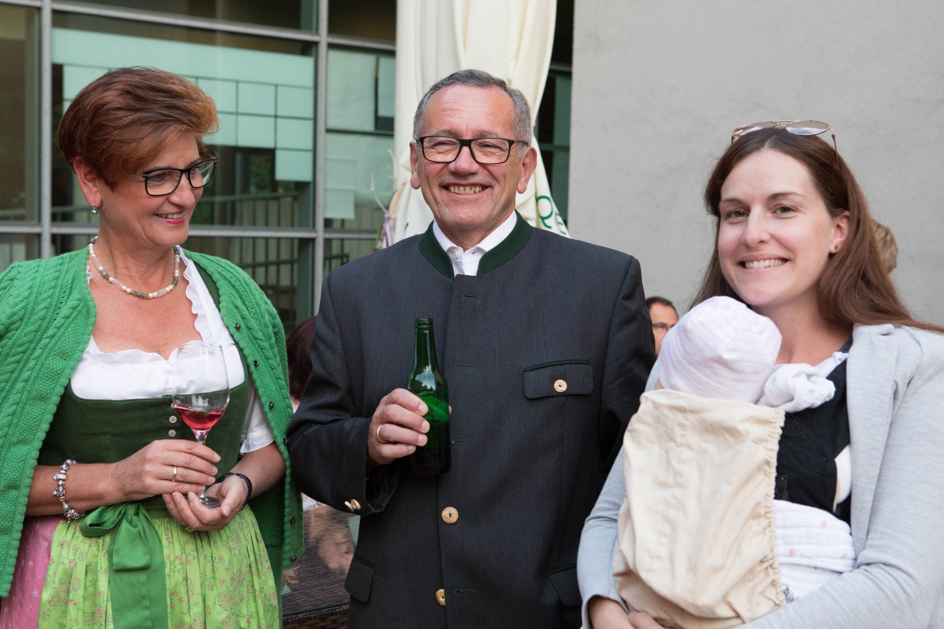 Ein Mann hält eine Flasche Wein und eine Frau ein Baby.