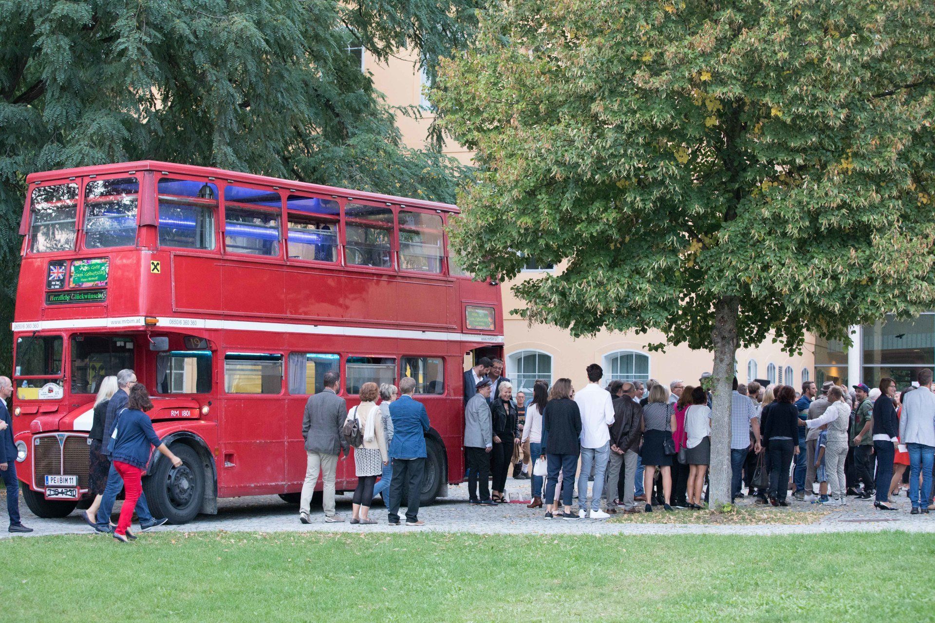 Eine Gruppe von Menschen steht um einen roten Doppeldeckerbus