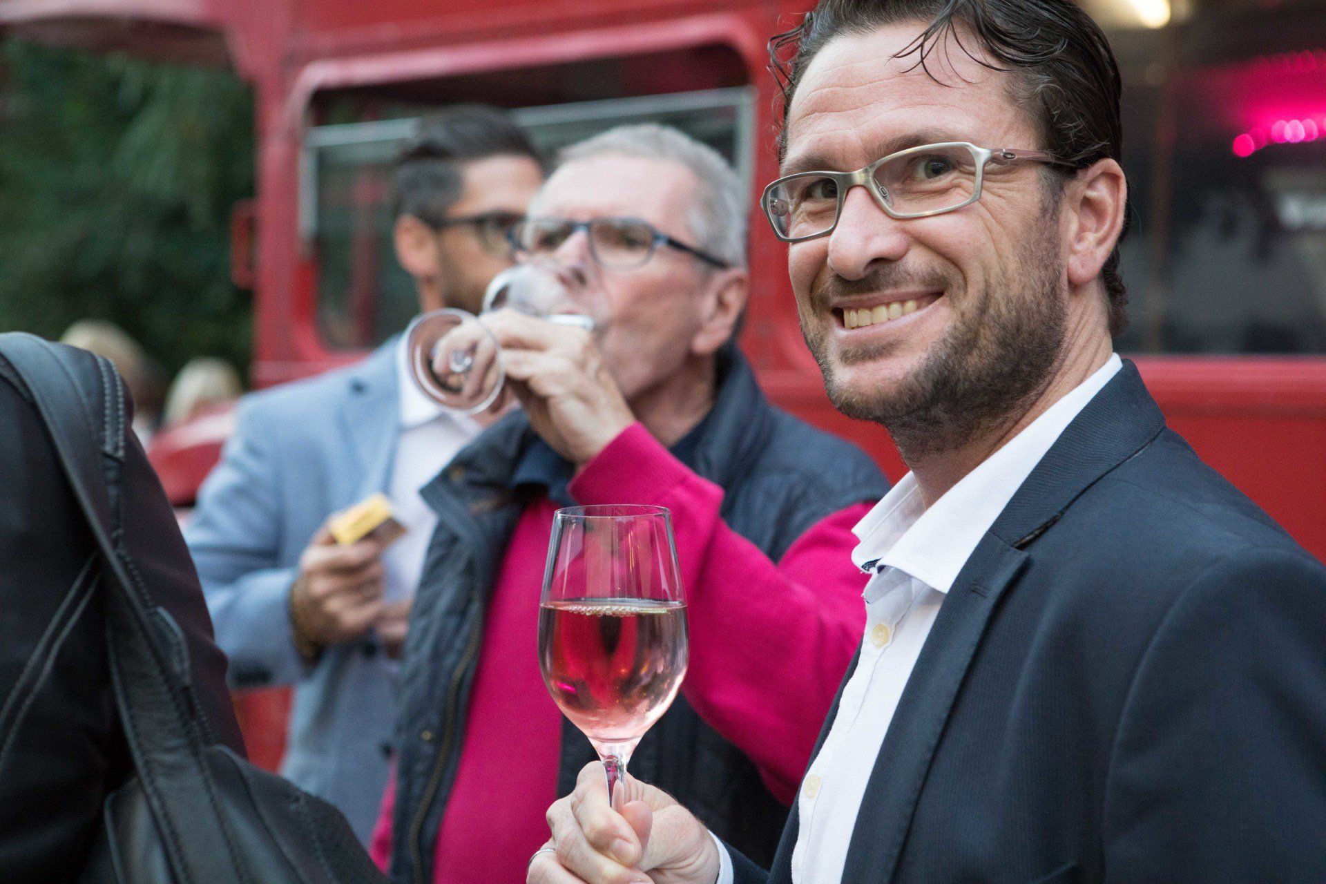 Ein Mann im Anzug hält ein Glas Wein in der Hand.