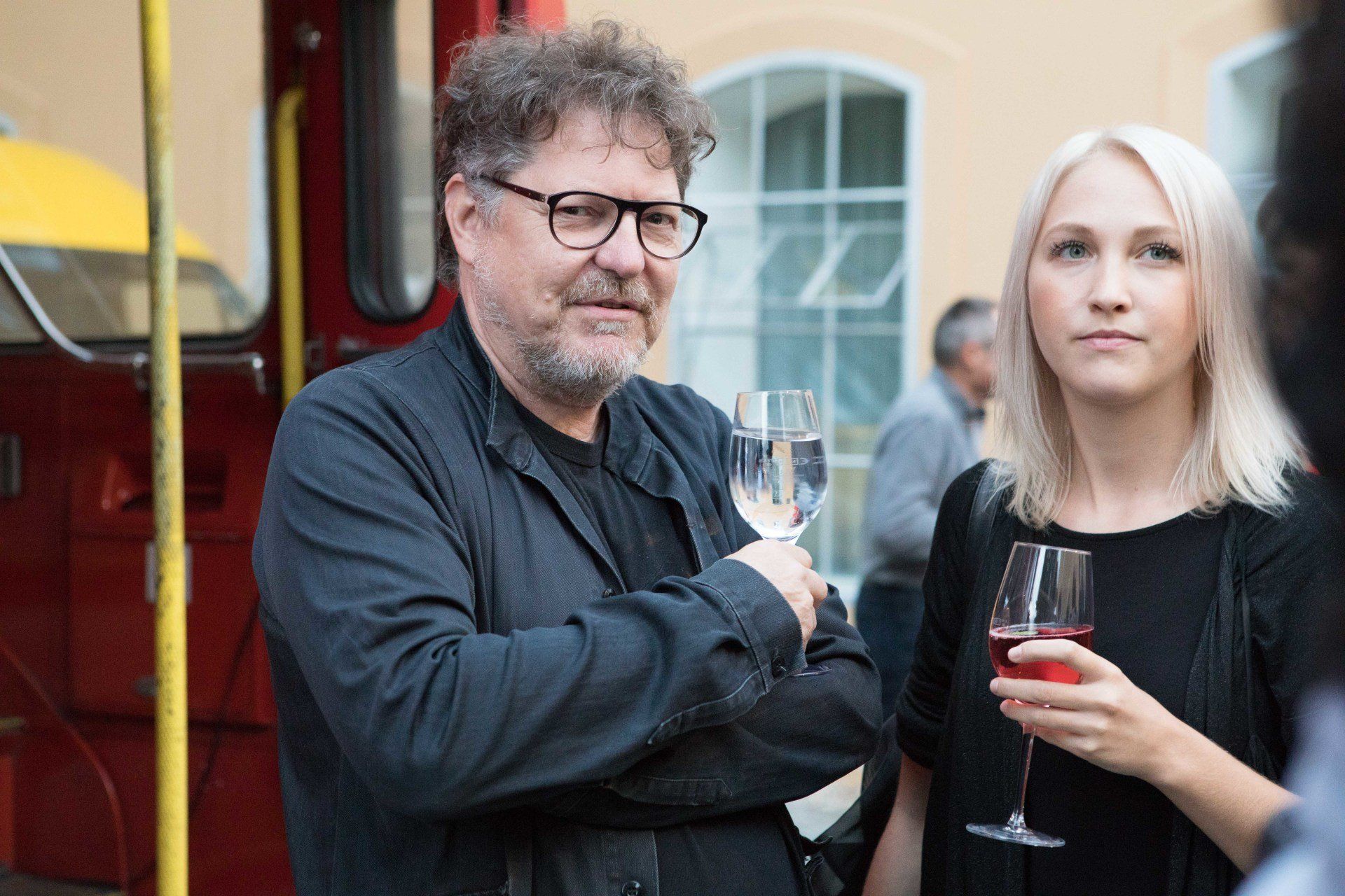Ein Mann und eine Frau stehen nebeneinander und halten Weingläser in der Hand.