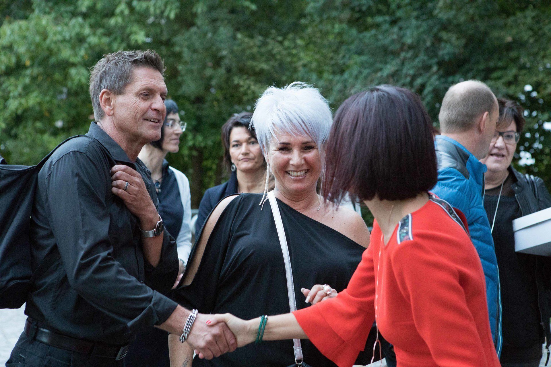 Ein Mann schüttelt einer Frau in einem roten Kleid die Hand.