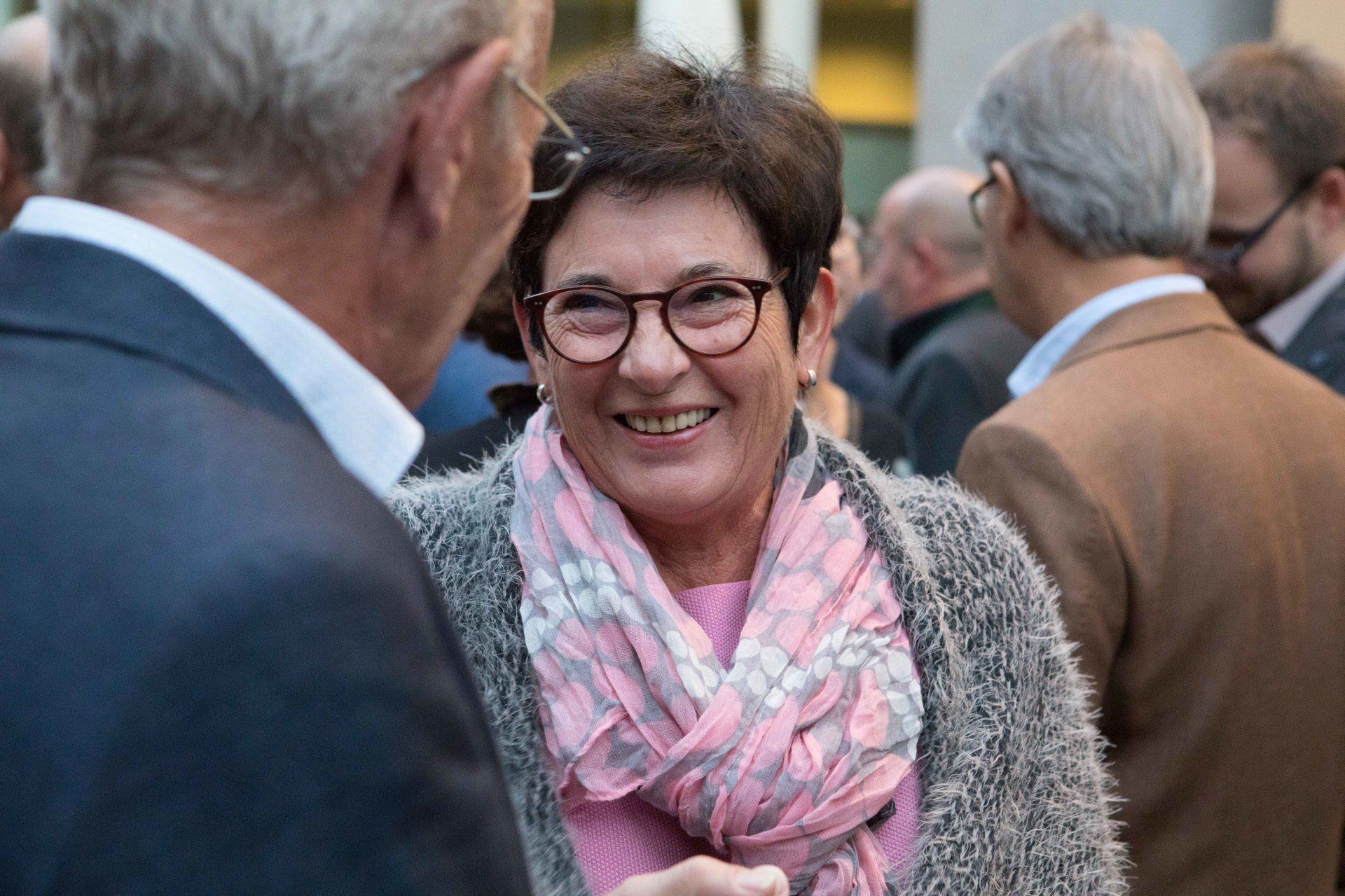 Eine Frau mit Brille und rosa Schal spricht mit einem Mann im Anzug.