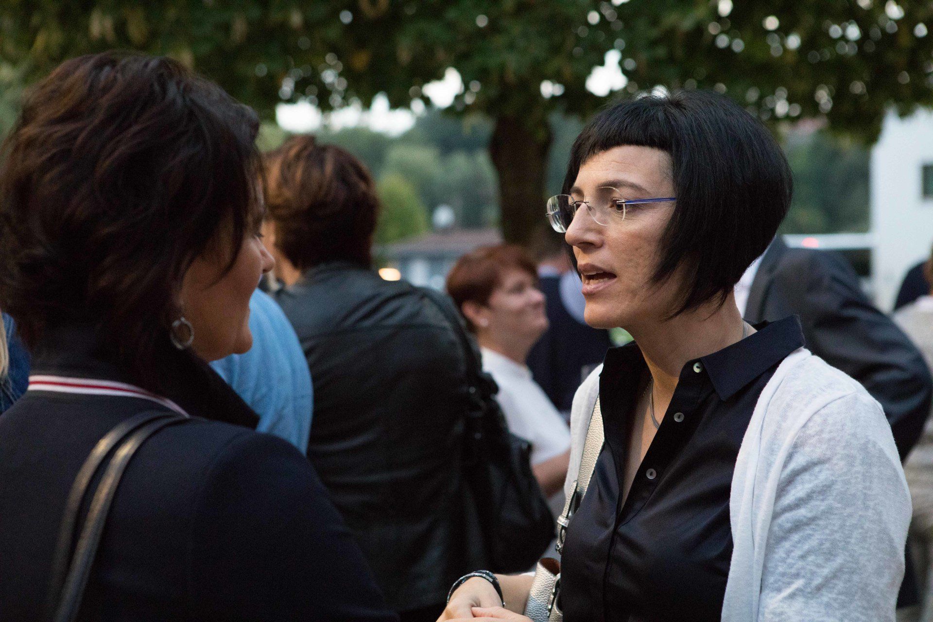 Eine Frau mit Brille spricht in einer Menschenmenge mit einer anderen Frau.