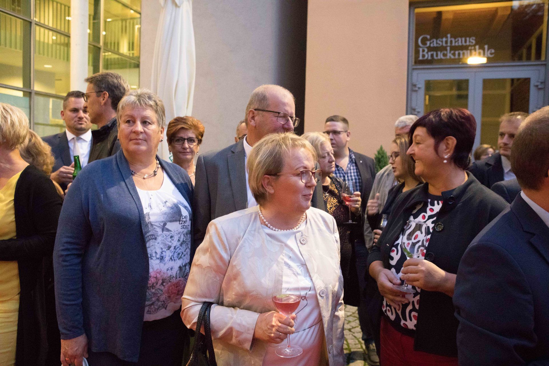 Eine Gruppe von Menschen steht mit Weingläsern in den Händen vor einem Gebäude.