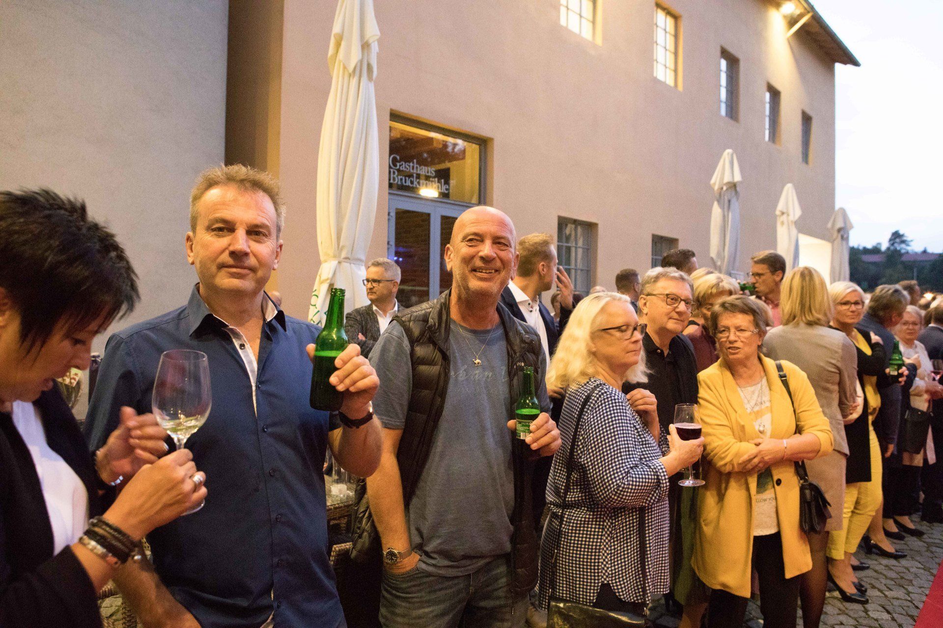 Eine Gruppe von Menschen steht vor einem Gebäude und trinkt Wein.
