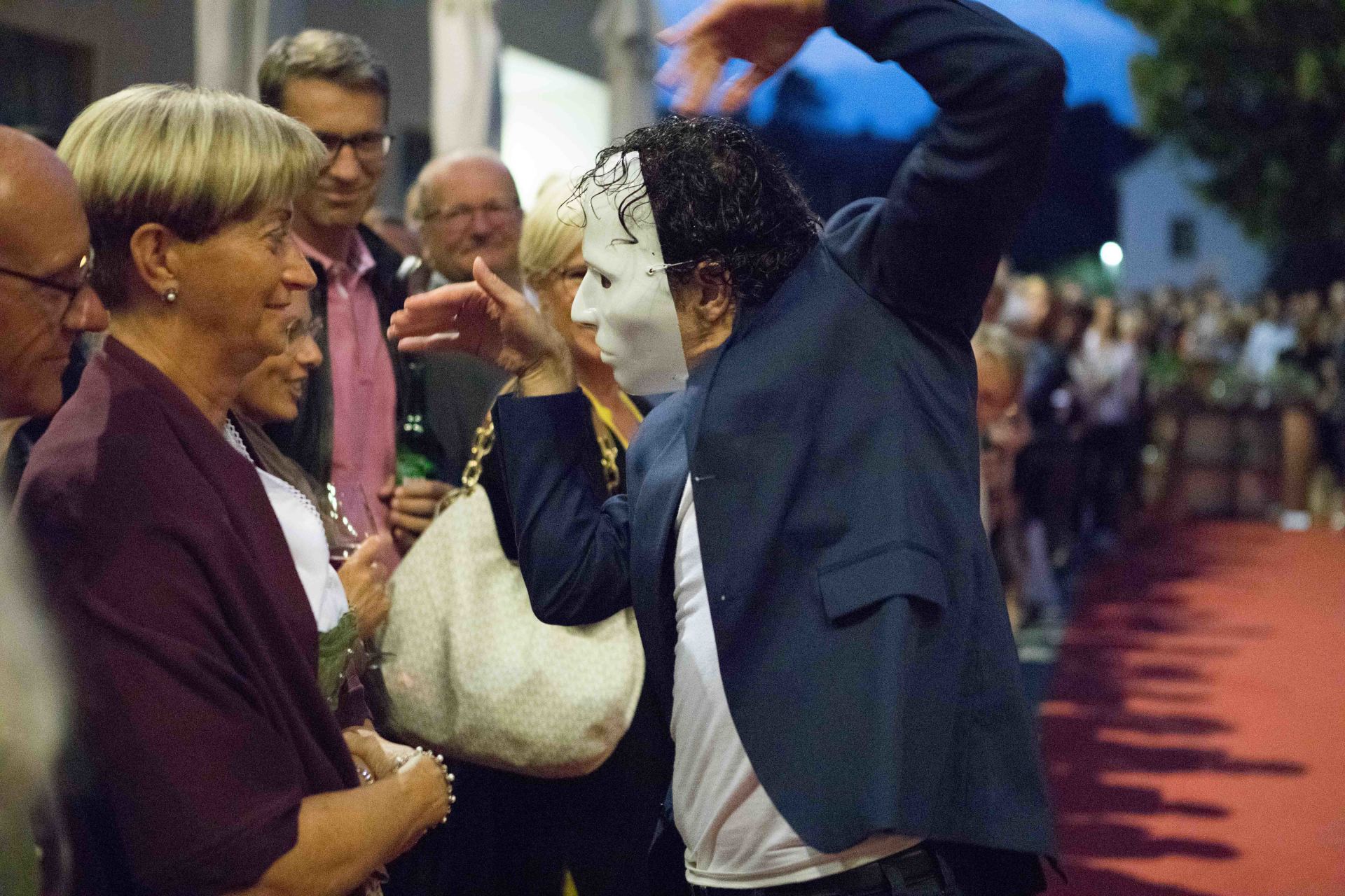 Ein Mann mit einer Maske steht in einer Menschenmenge.