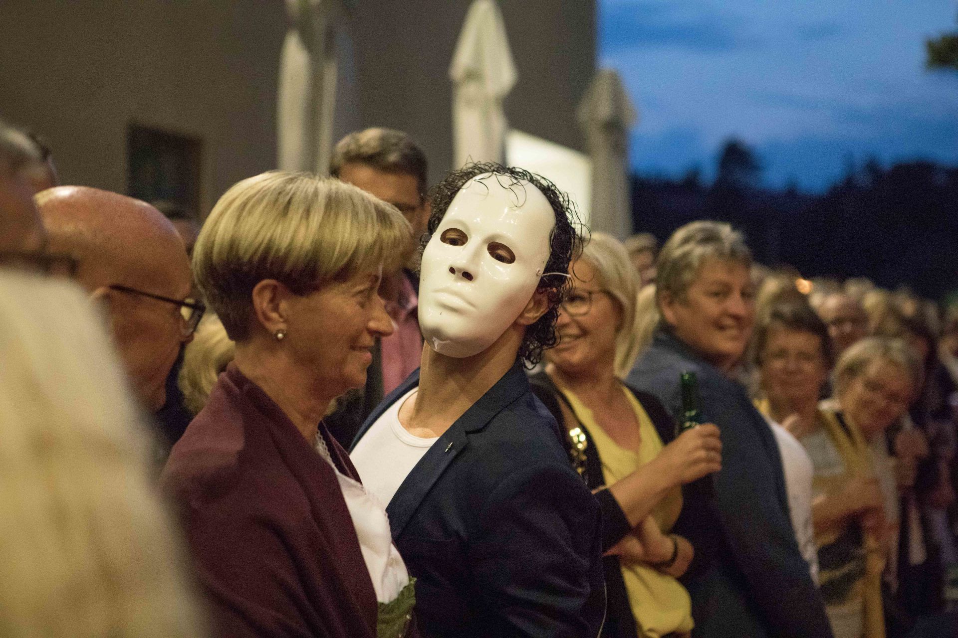 Ein Mann mit einer weißen Maske steht in einer Menschenmenge.