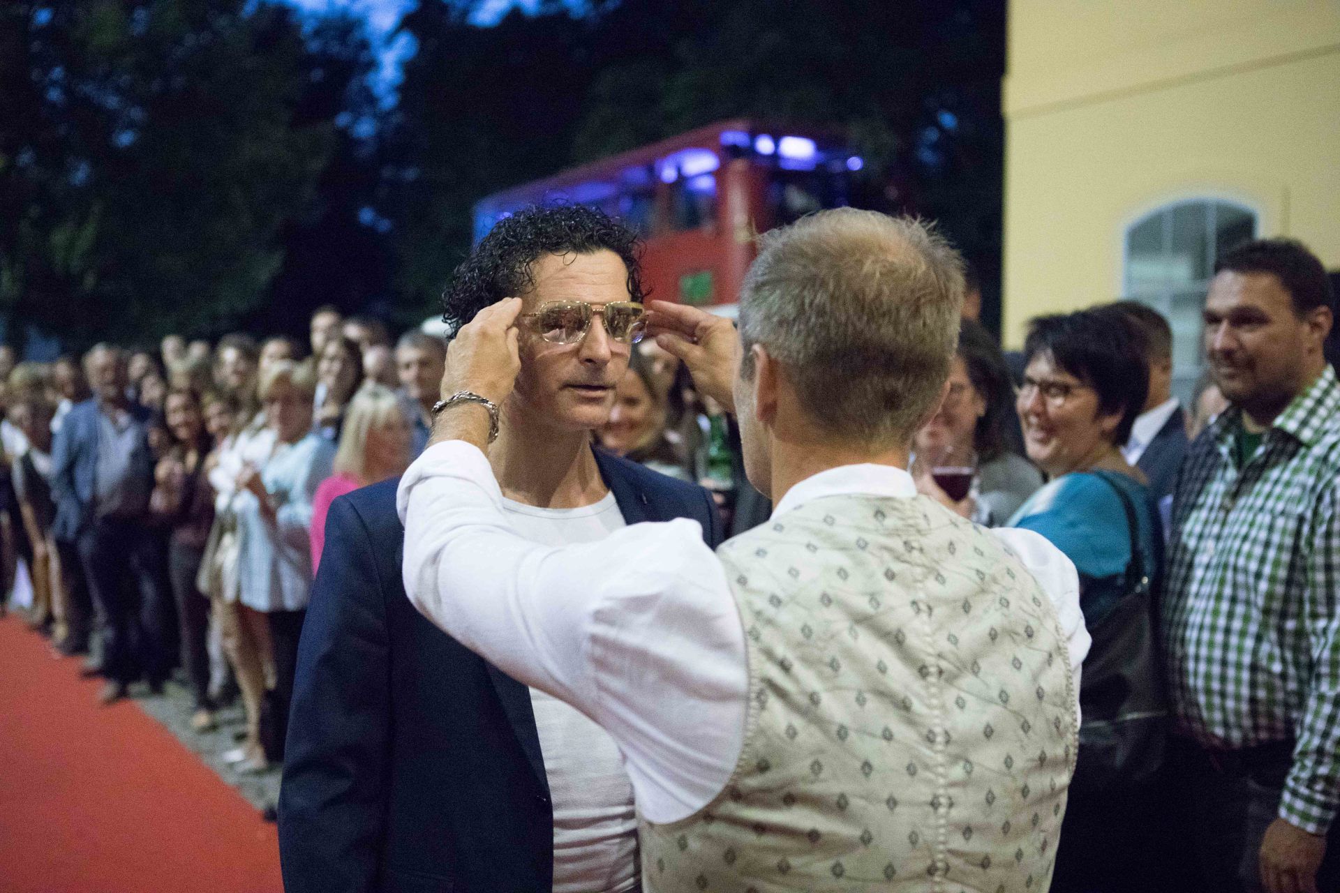 Ein Mann rückt vor einer Menschenmenge die Brille eines anderen Mannes zurecht.