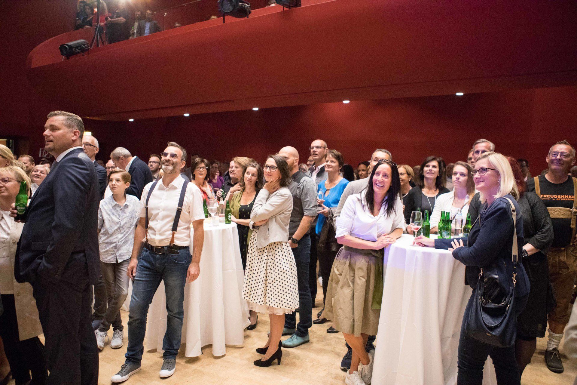 Eine Gruppe von Menschen steht in einem großen Raum um Tische herum.