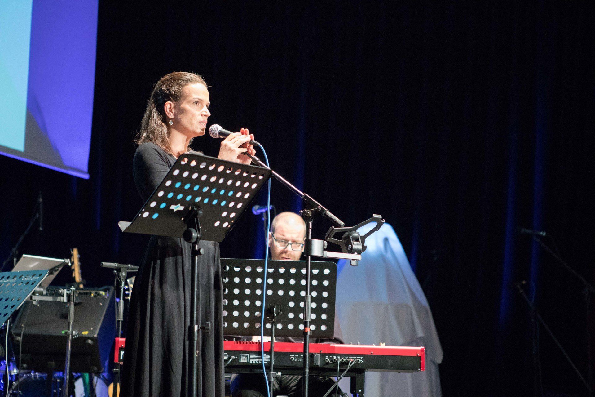Auf einer Bühne singt eine Frau in ein Mikrofon, während ein Mann Keyboard spielt.