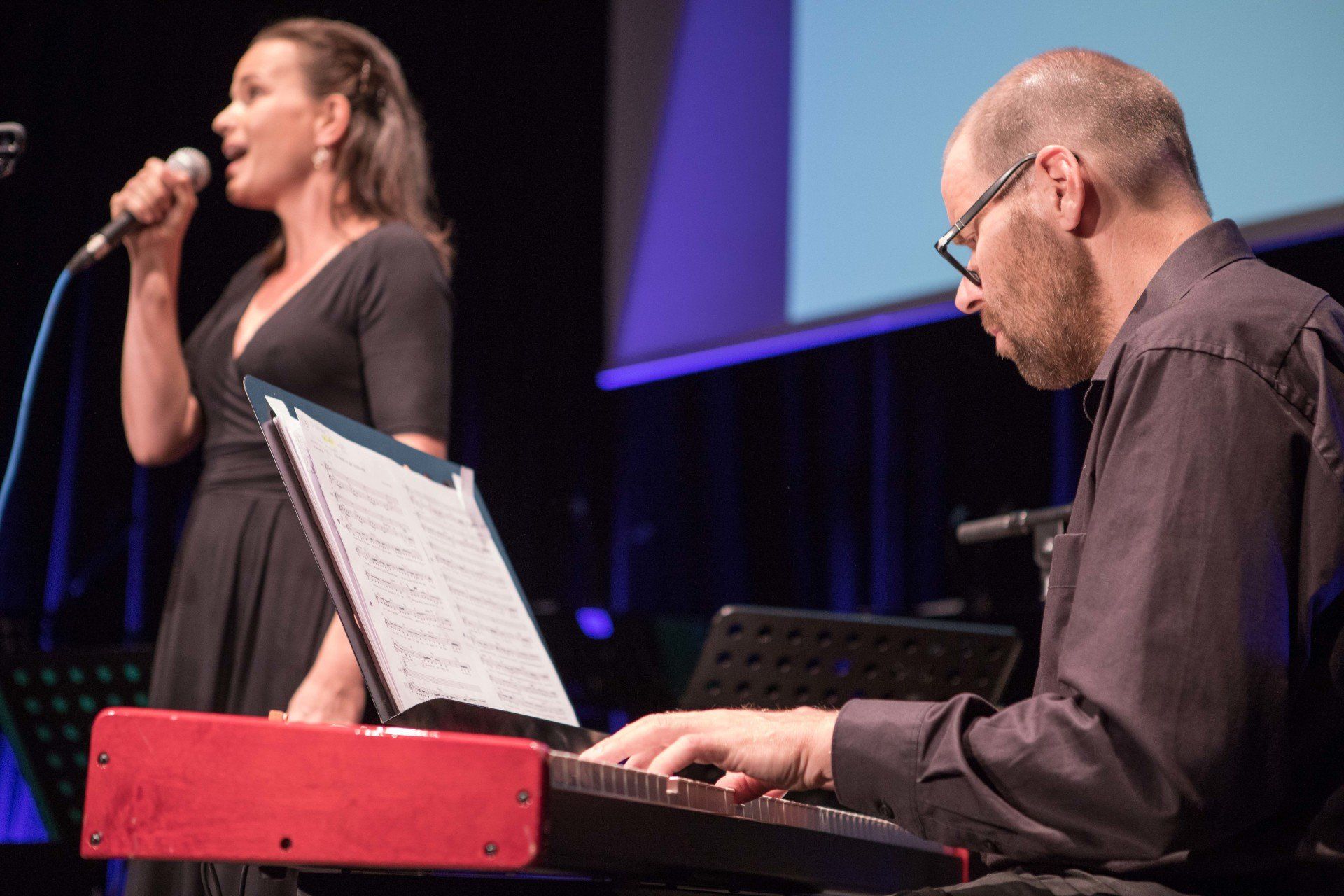 Ein Mann spielt Keyboard, während eine Frau in ein Mikrofon singt.