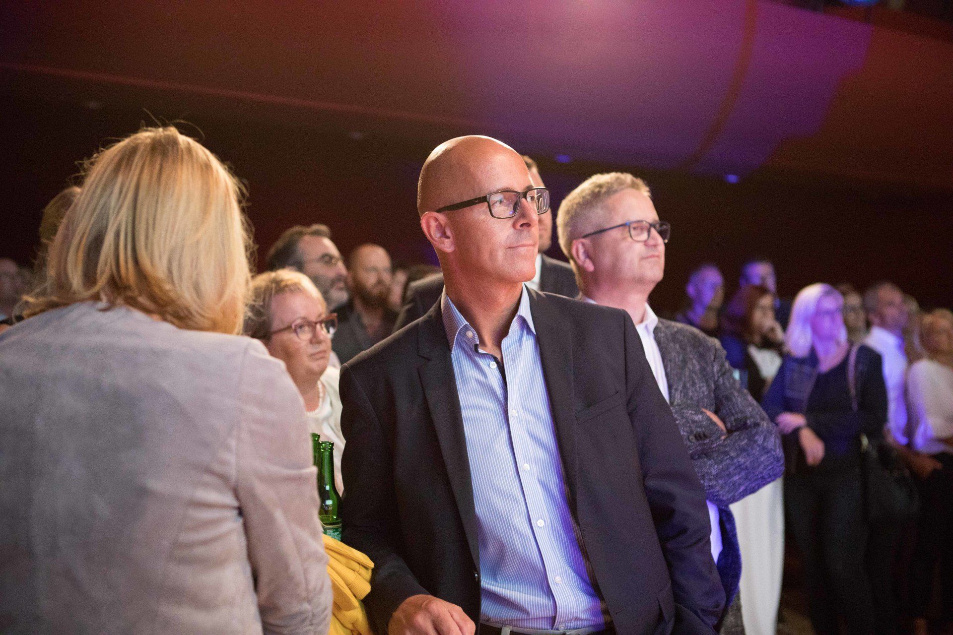 Ein Mann in Anzug und Brille steht vor einer Menschenmenge.