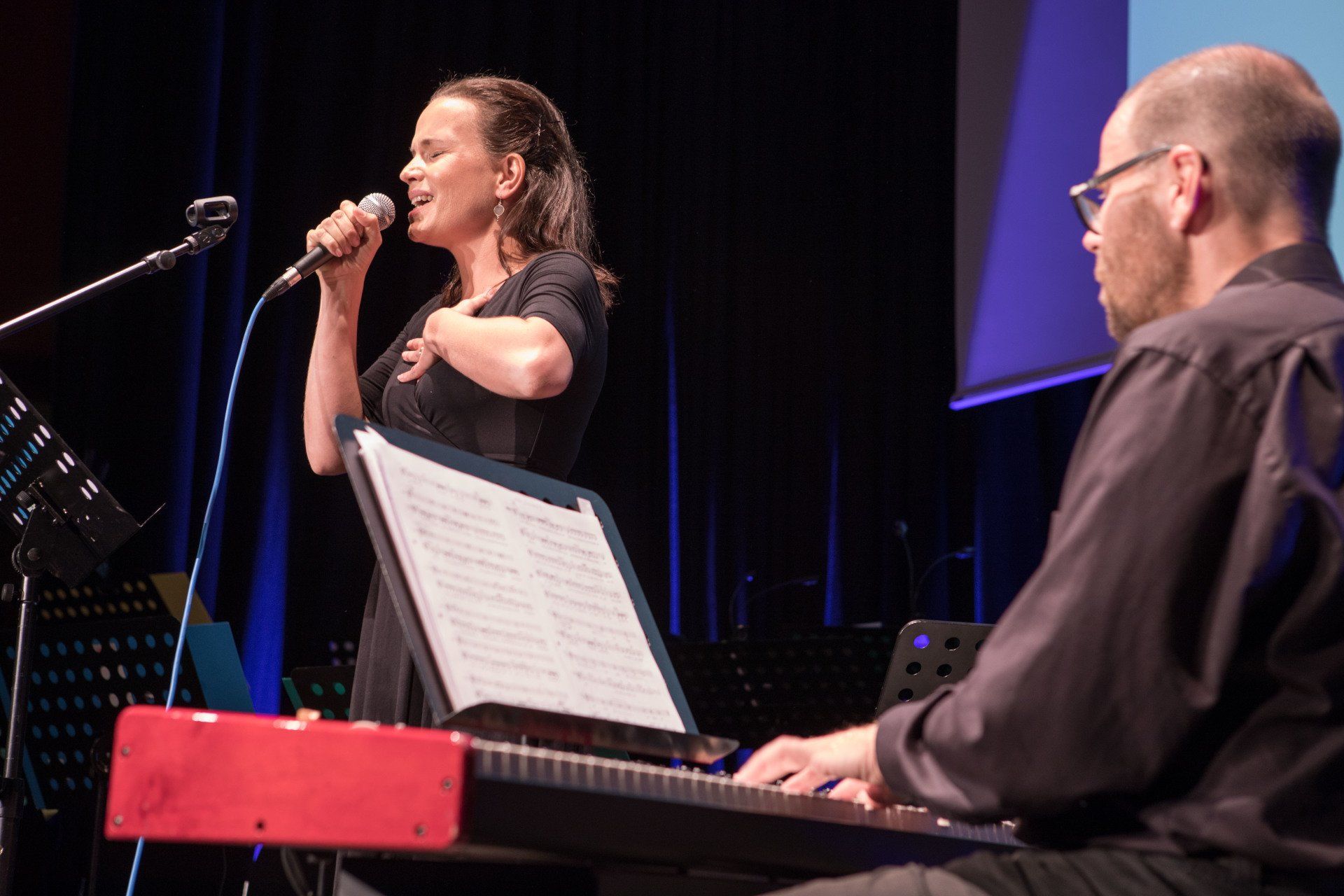 Eine Frau, die in ein Mikrofon singt, während ein Mann Keyboard spielt