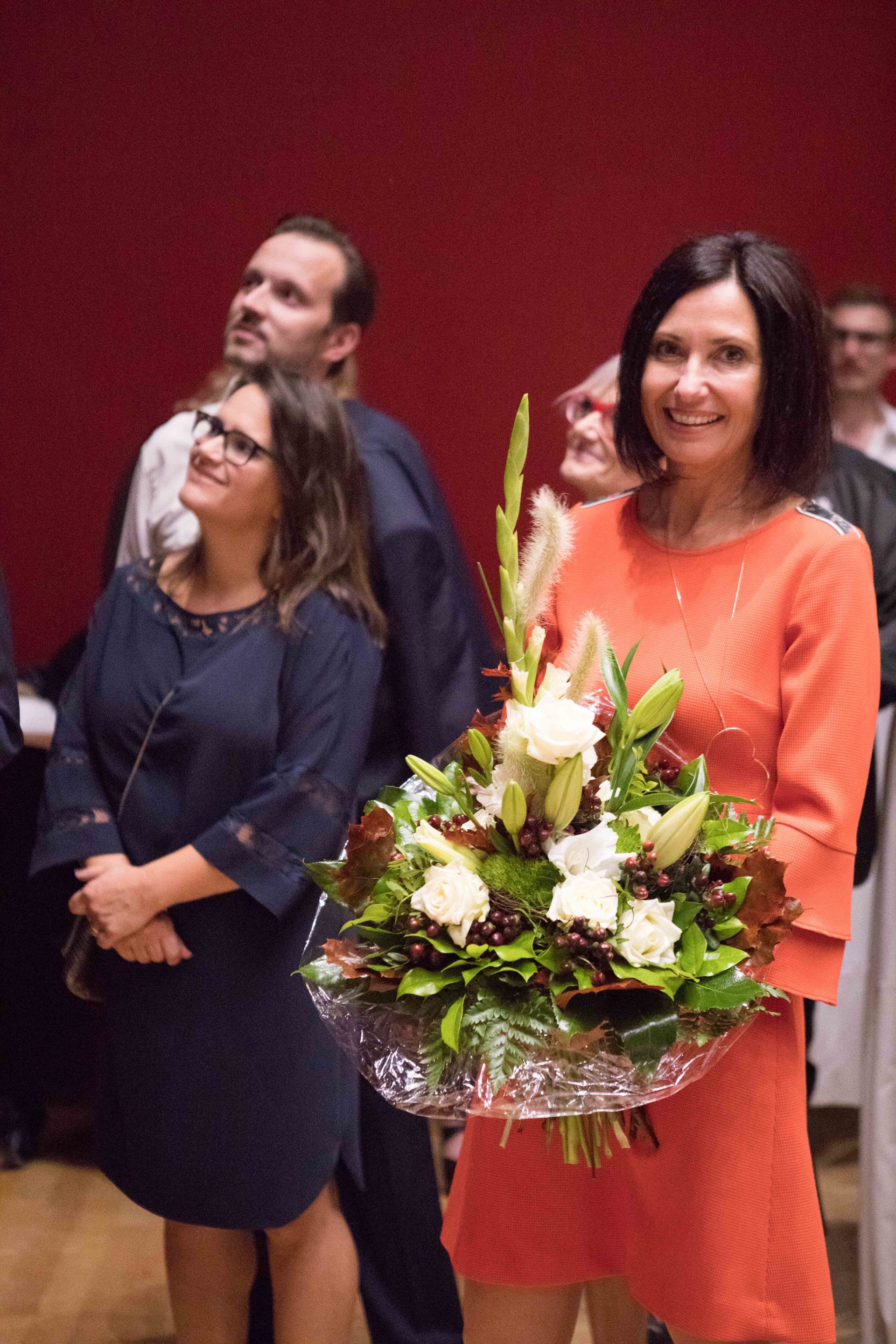Eine Frau in einem orangefarbenen Kleid hält einen Blumenstrauß.