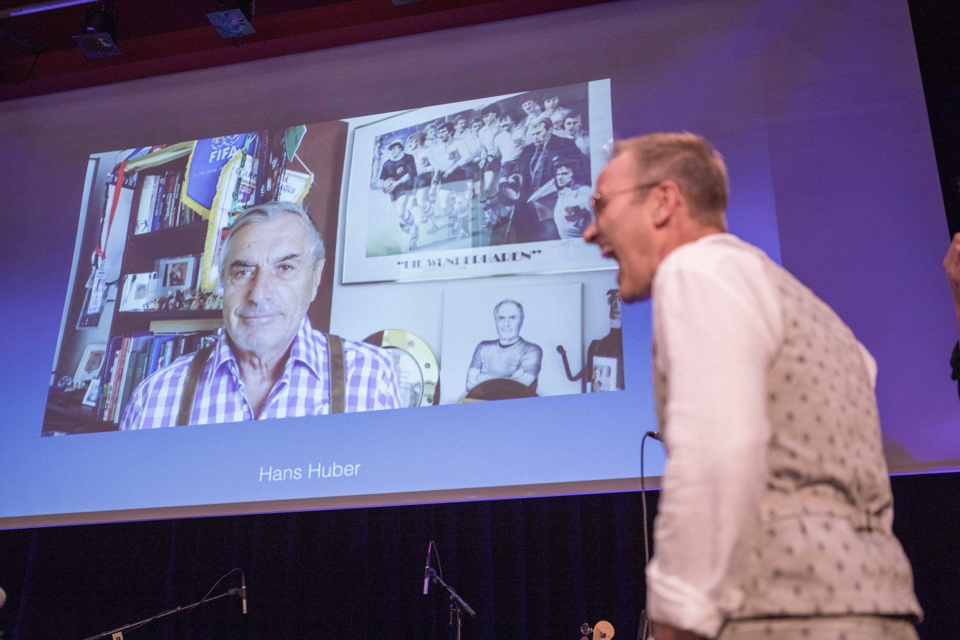 Ein Mann steht vor einem großen Bildschirm, auf dem das Bild eines Mannes zu sehen ist.