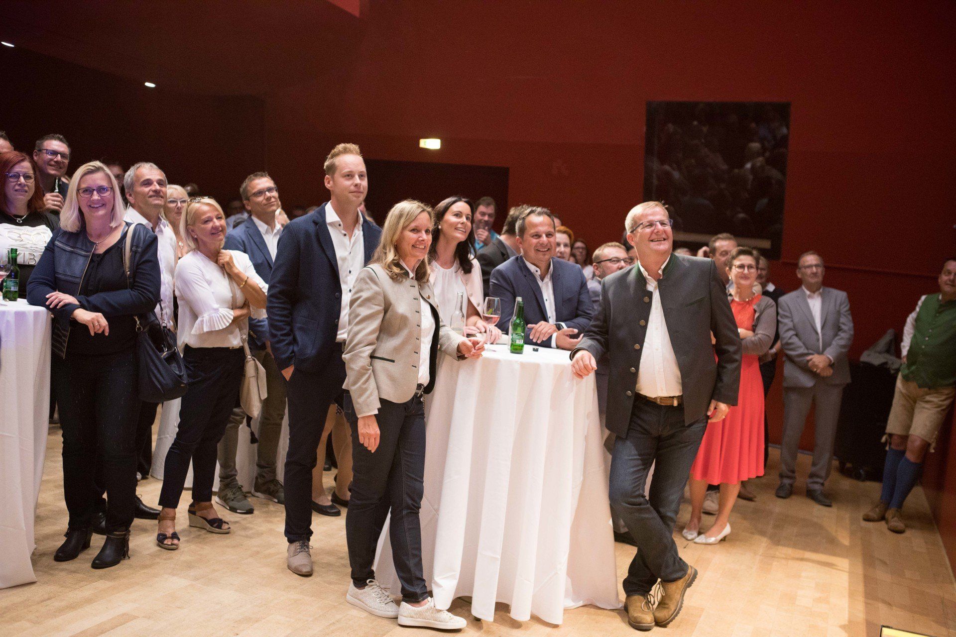 Eine Gruppe von Menschen steht in einem Raum um Tische herum.