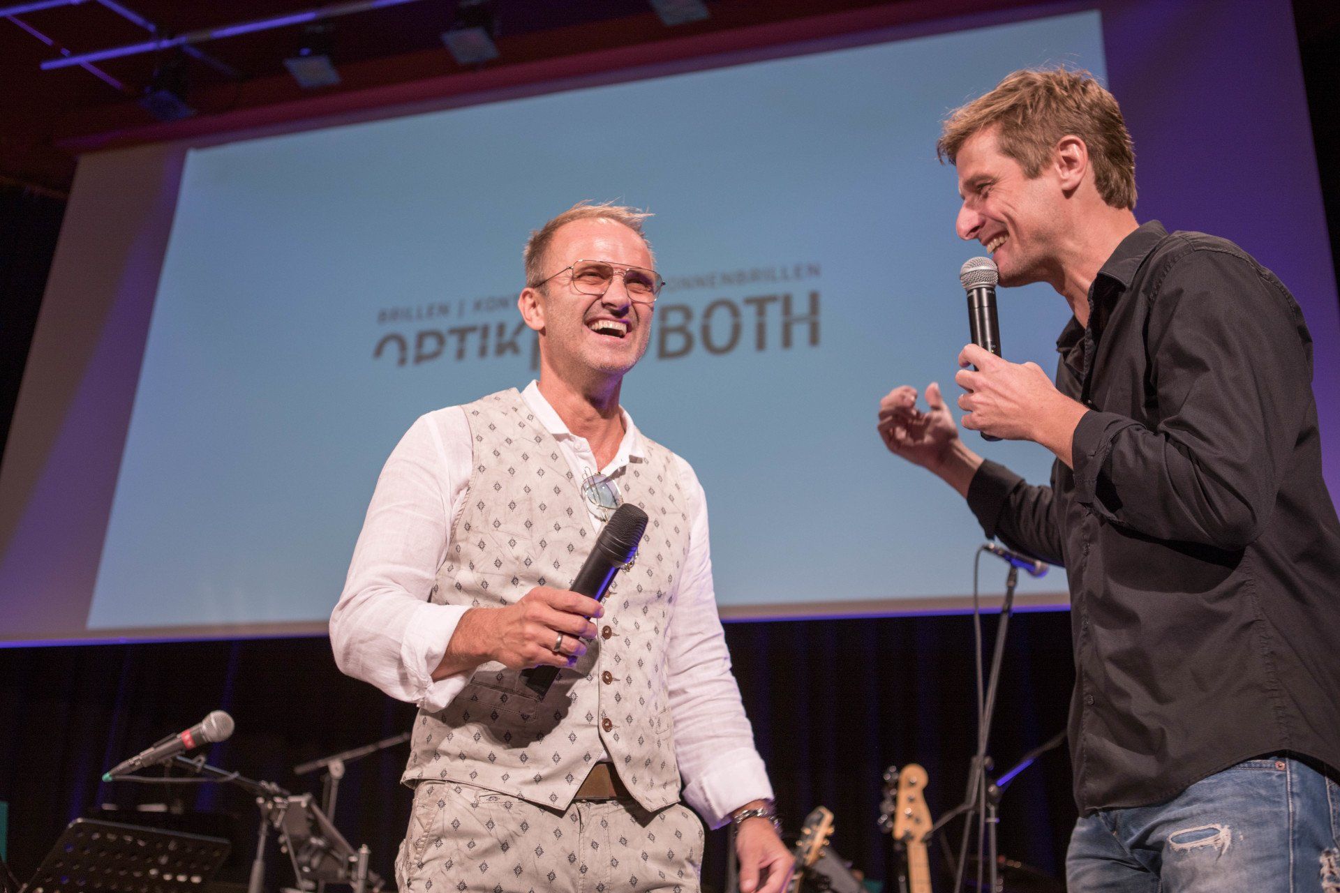 Zwei Männer stehen auf einer Bühne und sprechen in Mikrofone.