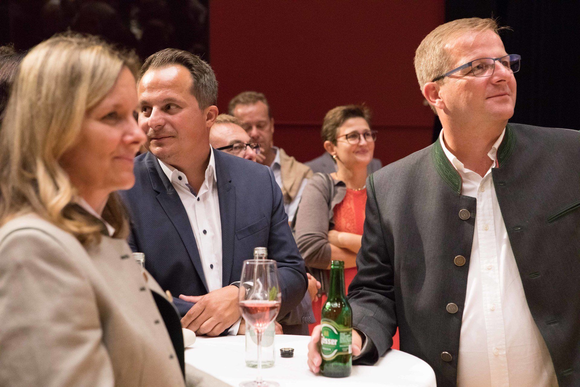 Eine Gruppe von Leuten sitzt mit einer Flasche Bier um einen Tisch herum.