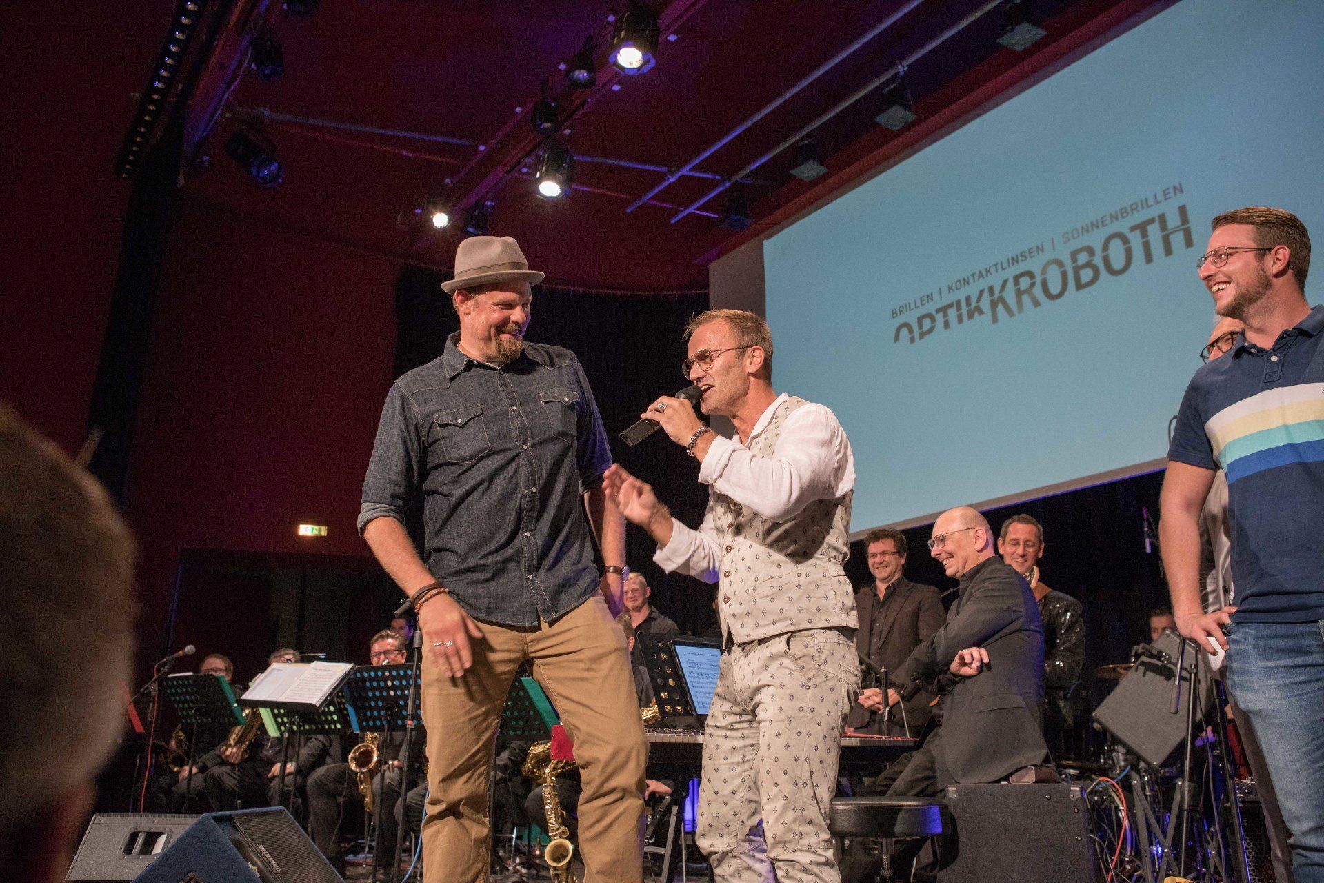 Eine Gruppe von Männern steht auf einer Bühne und unterhält sich miteinander.