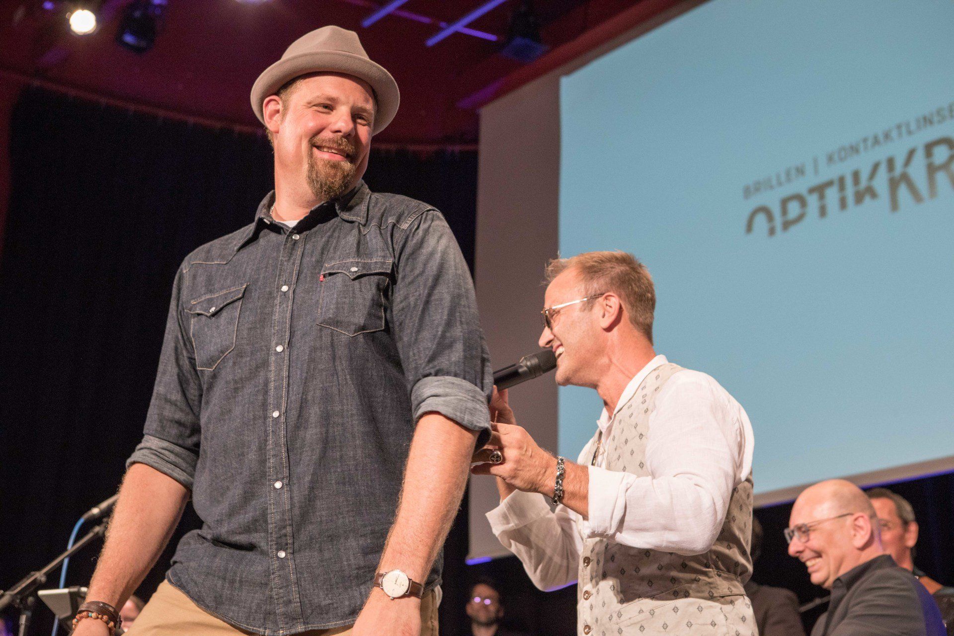 Ein Mann mit Hut steht neben einem anderen Mann, der ein Mikrofon hält.