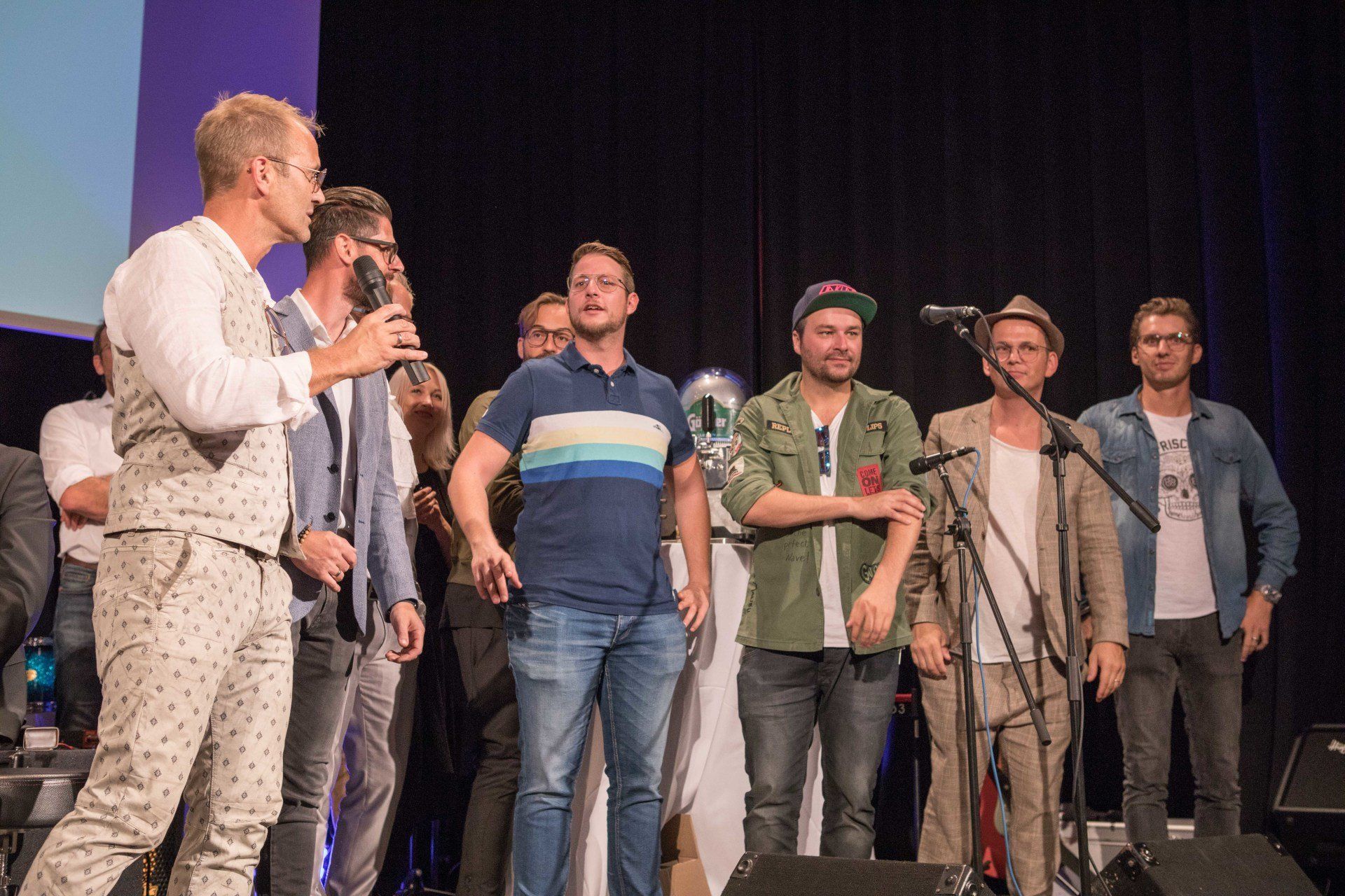 Eine Gruppe Männer steht auf einer Bühne vor Mikrofonen.