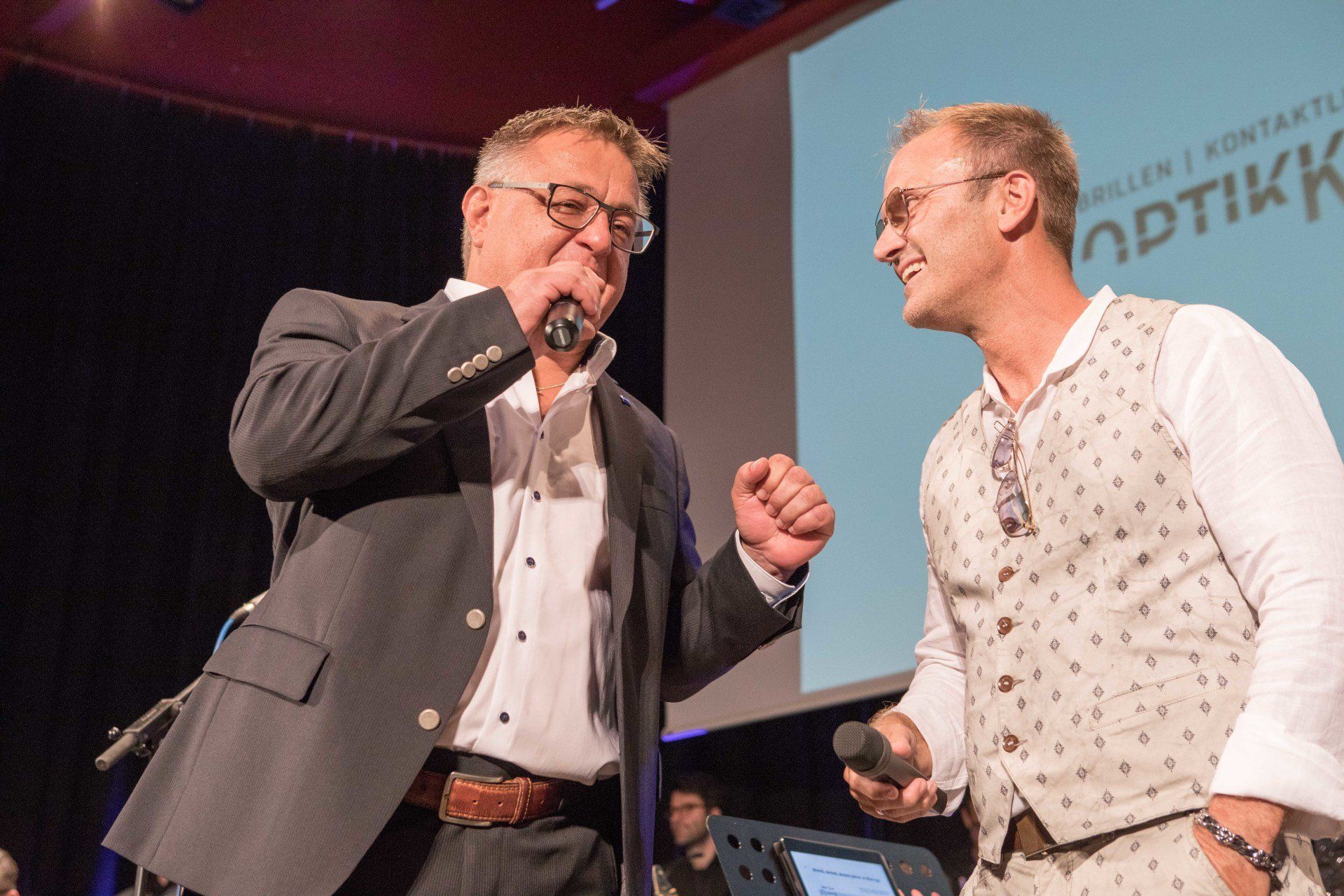 Zwei Männer singen auf einer Bühne in Mikrofone.