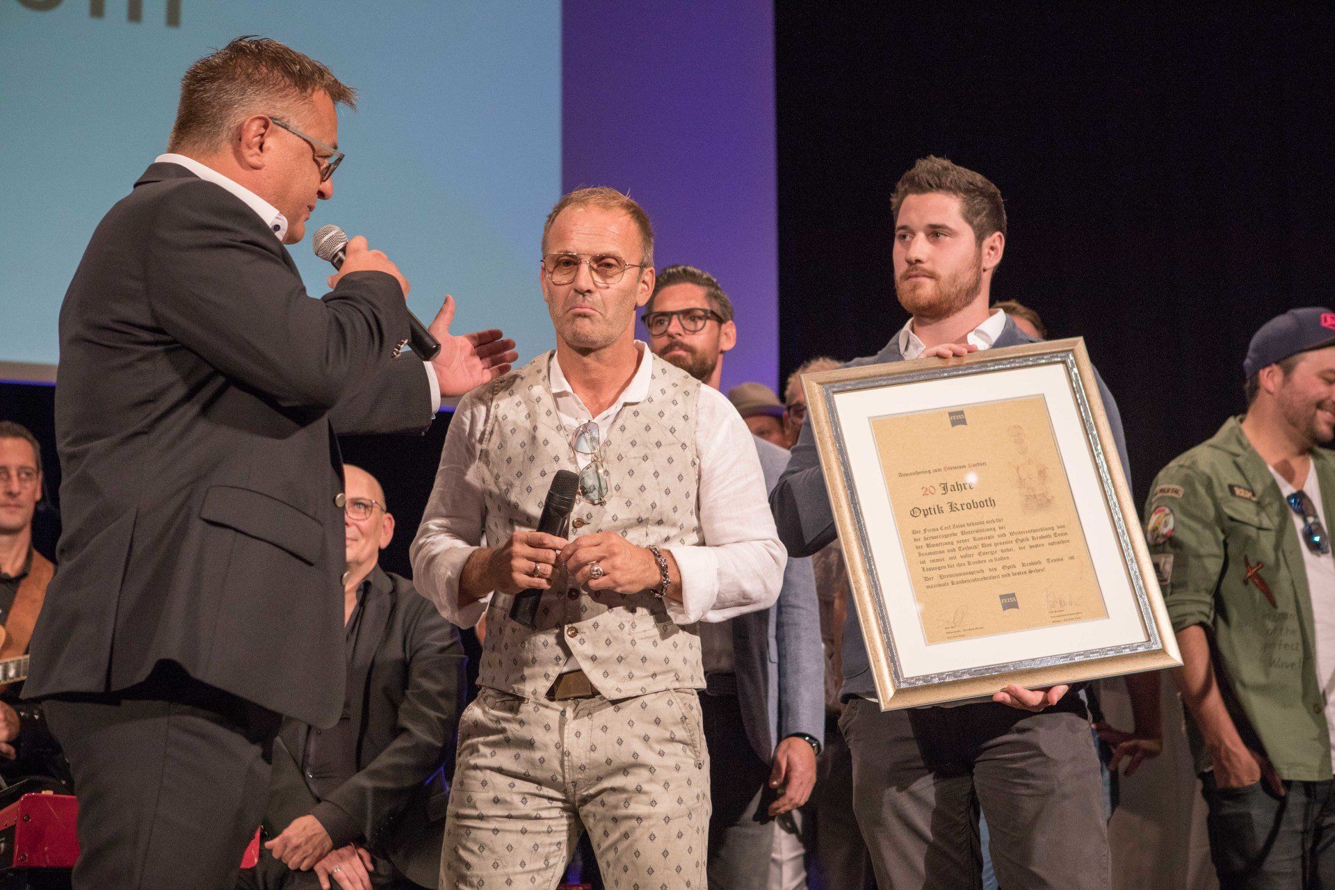 Eine Gruppe von Männern steht auf einer Bühne und hält eine gerahmte Urkunde in den Händen.