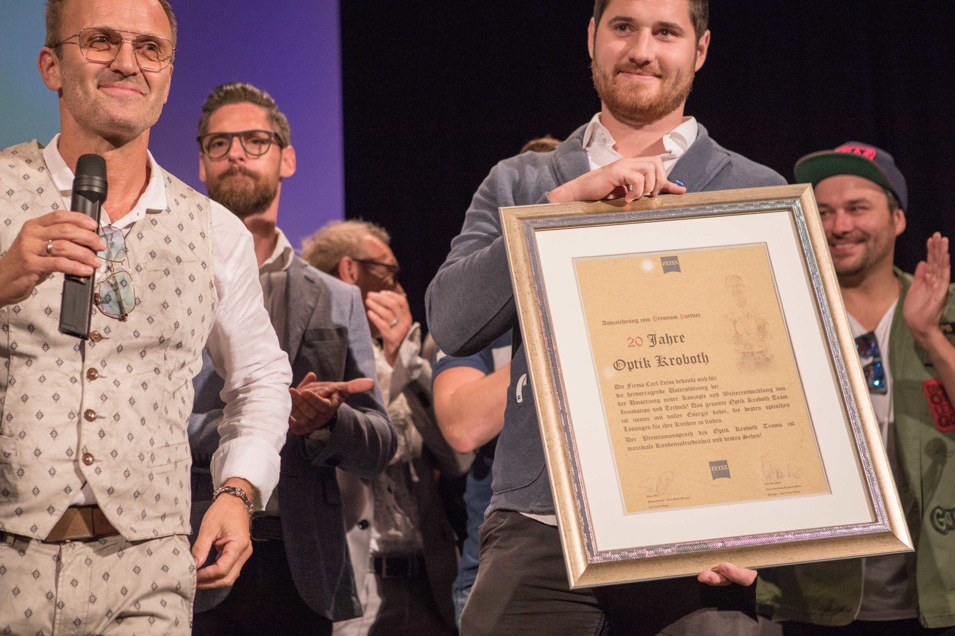 Ein Mann hält vor einer Gruppe von Männern ein gerahmtes Zertifikat in der Hand.
