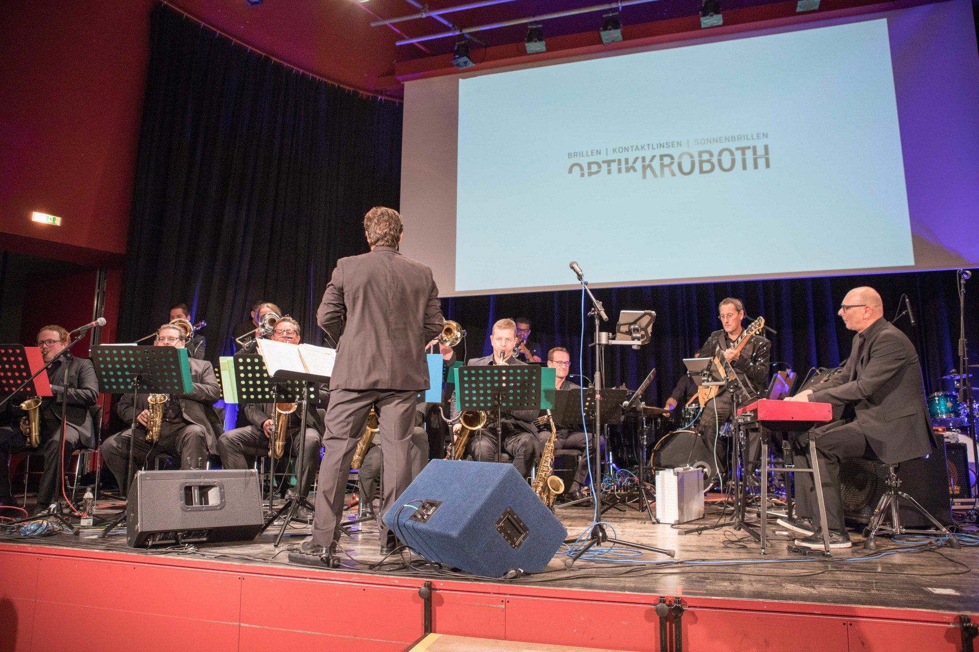 Ein Mann steht auf einer Bühne und leitet ein Orchester.