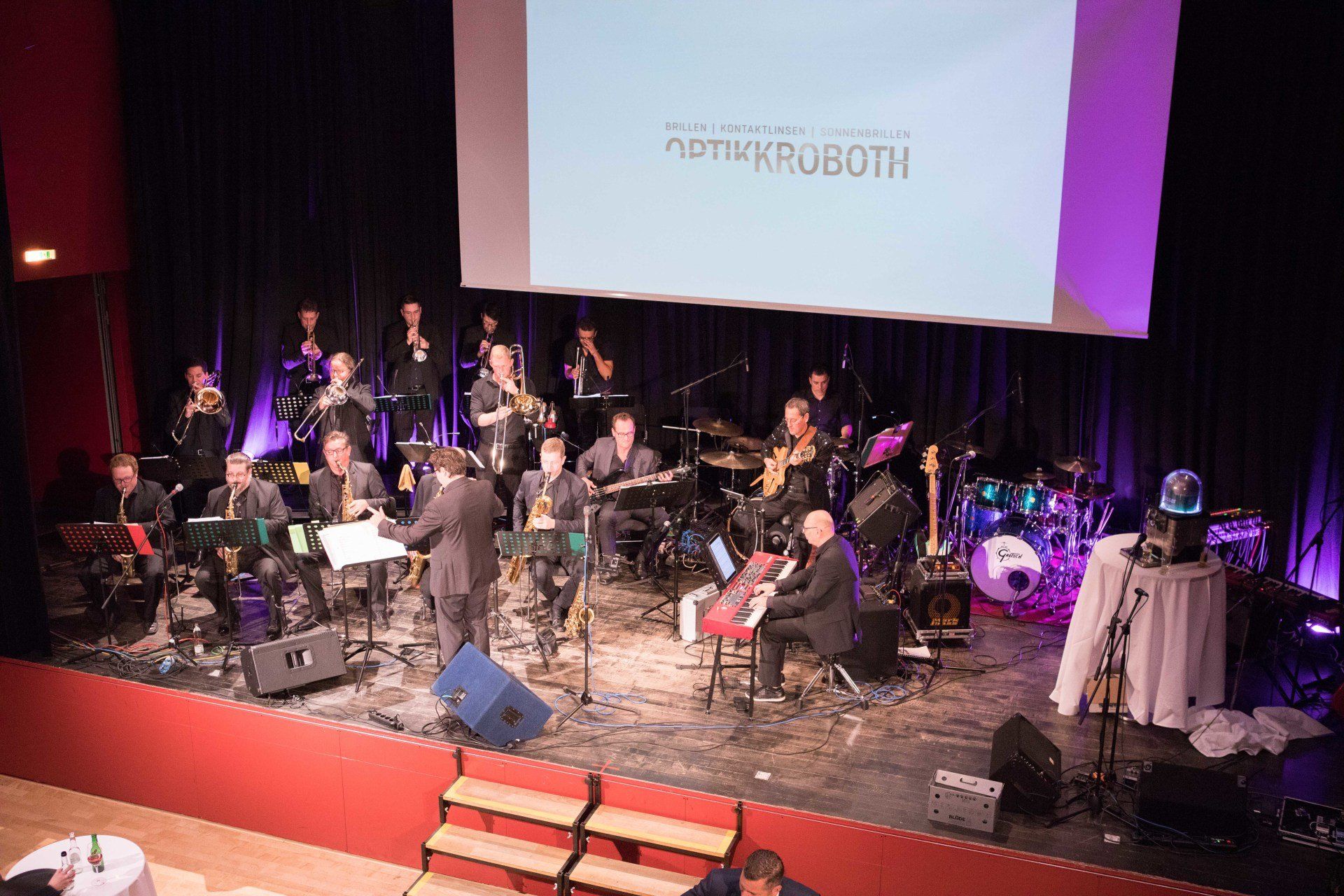 Auf einer Bühne spielt vor einer großen Leinwand ein großes Orchester.