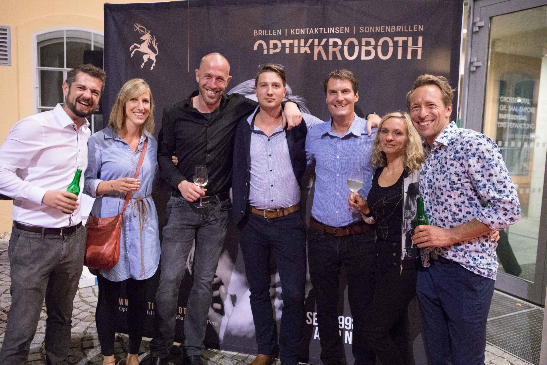 Eine Gruppe von Menschen posiert für ein Foto vor einem Schild mit der Aufschrift „optikkrobth“