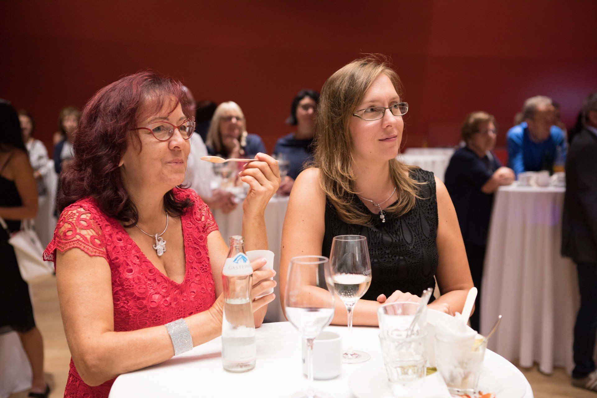 Zwei Frauen sitzen mit Weingläsern an einem Tisch.