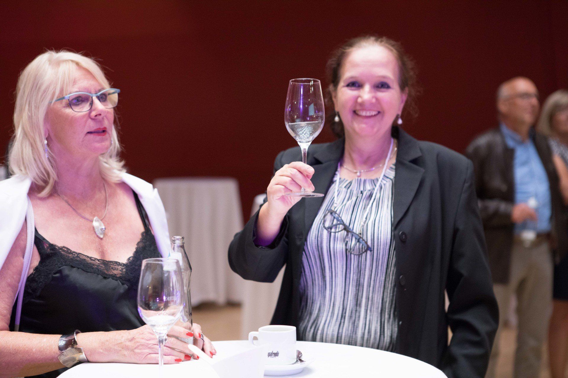 Zwei Frauen sitzen an einem Tisch und stoßen mit Weingläsern an.