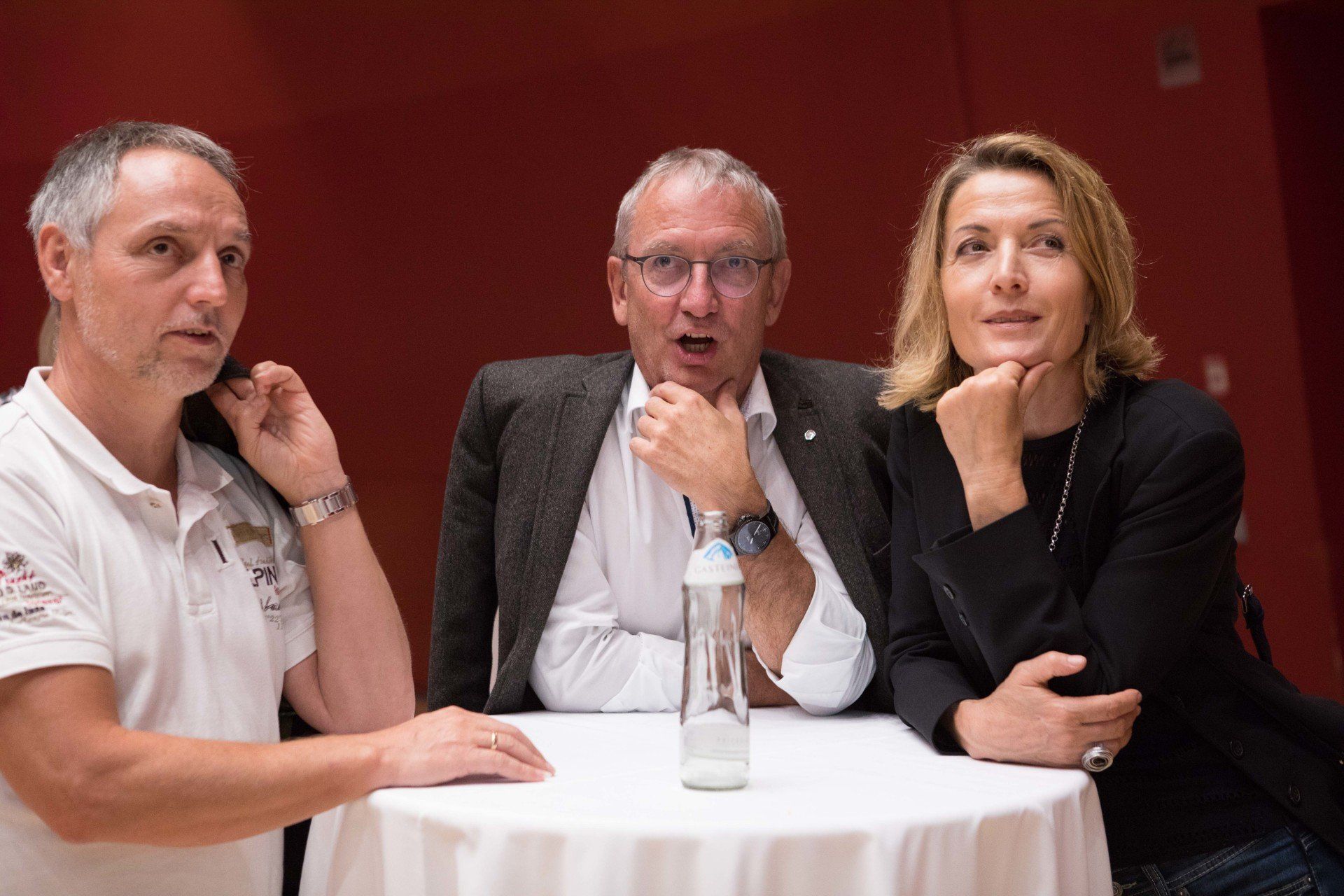 Ein Mann und zwei Frauen sitzen mit einer Flasche Wasser an einem Tisch.