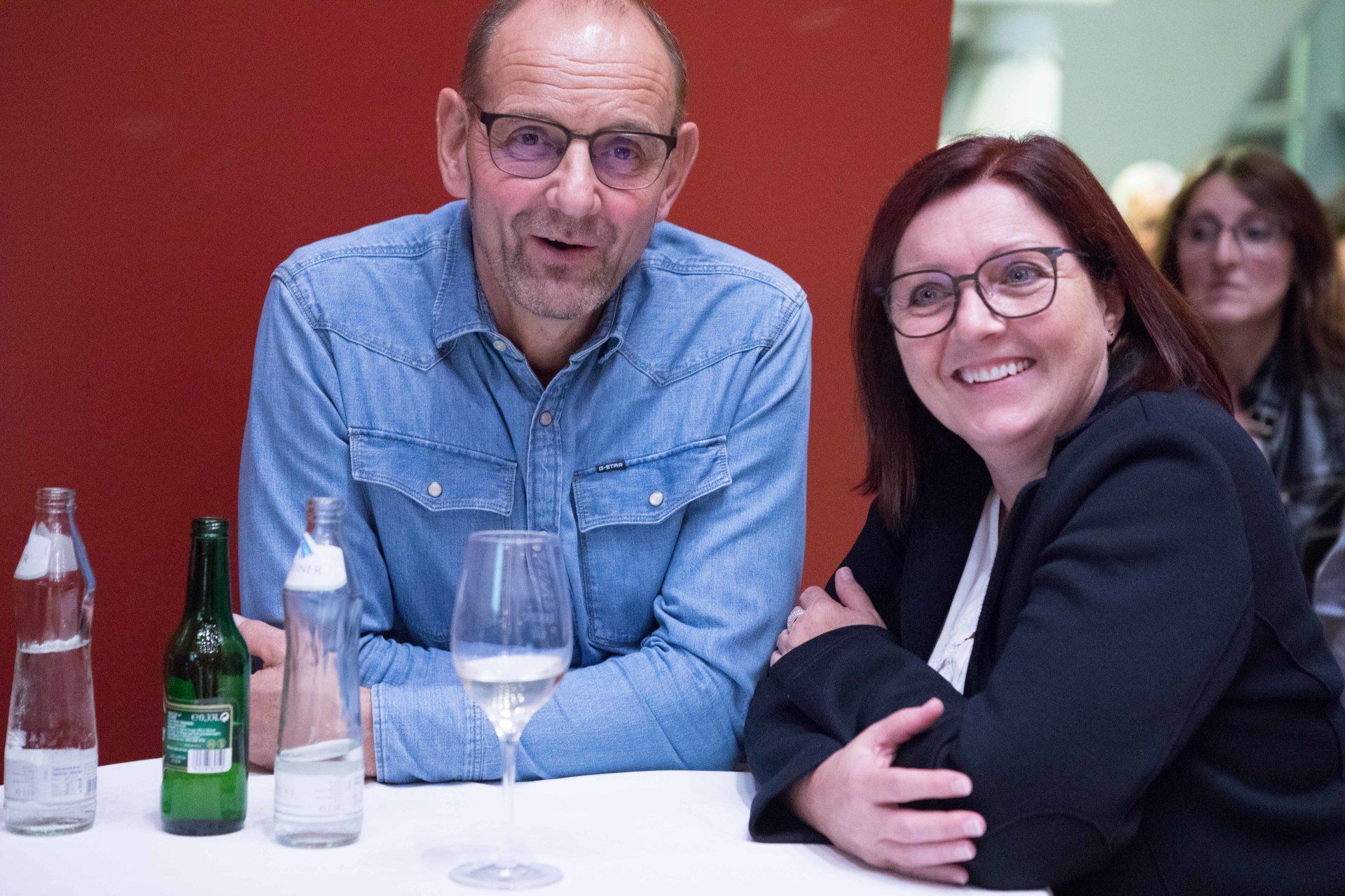 Ein Mann und eine Frau sitzen mit Weingläsern an einem Tisch.