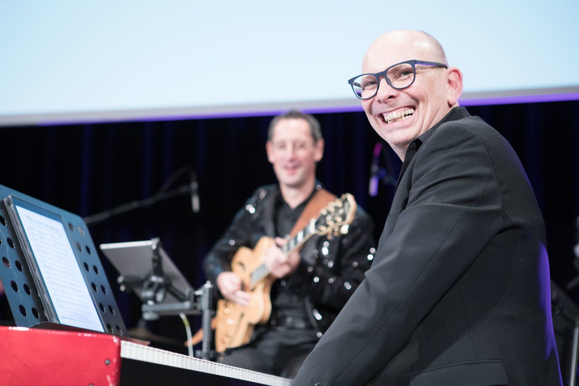 Ein Mann spielt Klavier und ein anderer Mann spielt Gitarre.
