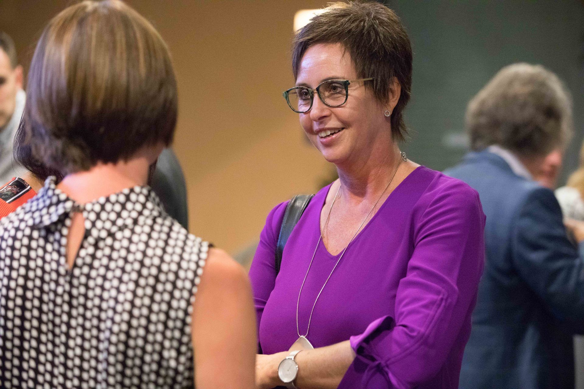 Eine Frau in einem lila Hemd und mit Brille spricht mit einer anderen Frau.