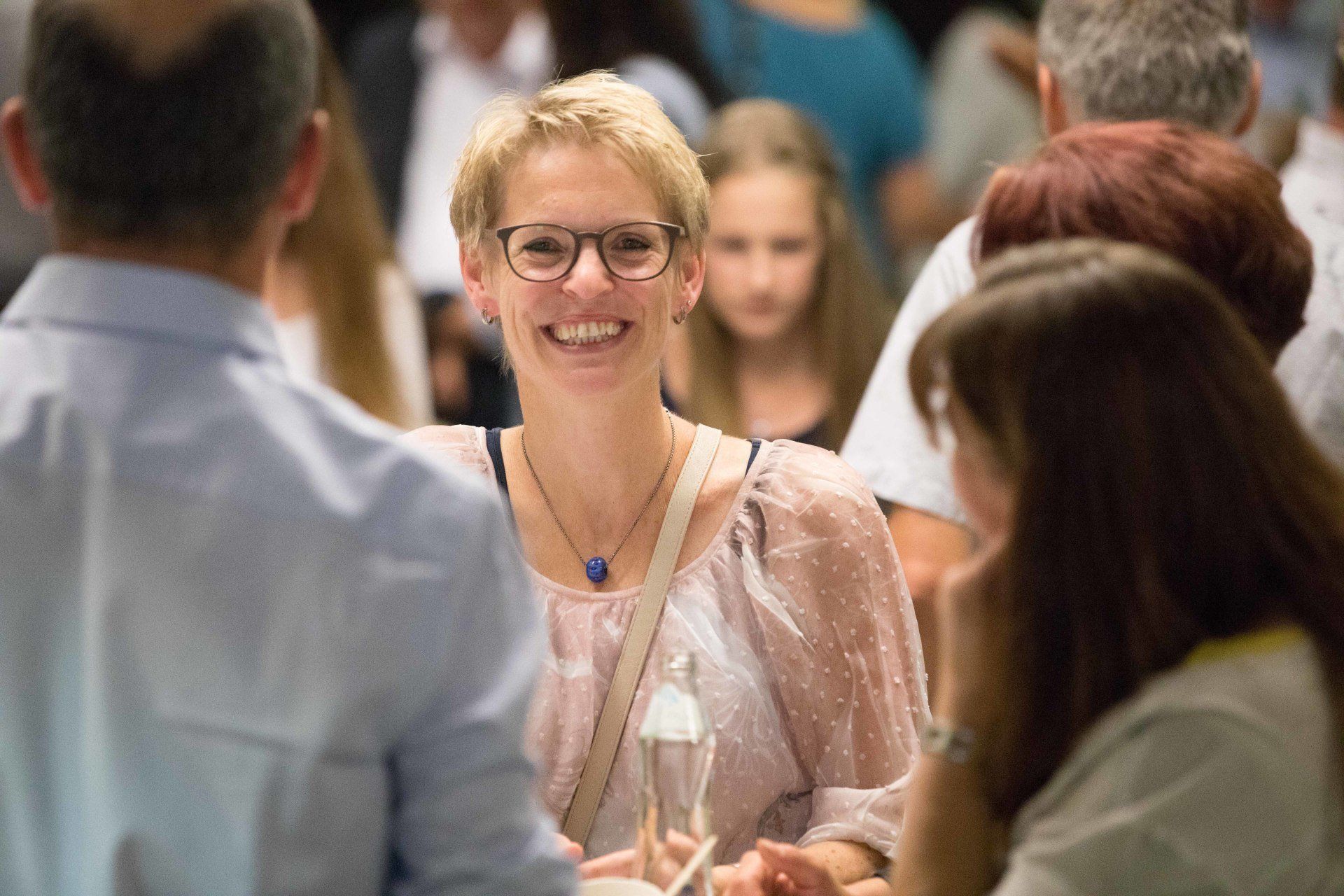 Eine Frau mit Brille lächelt in einer Menschenmenge.