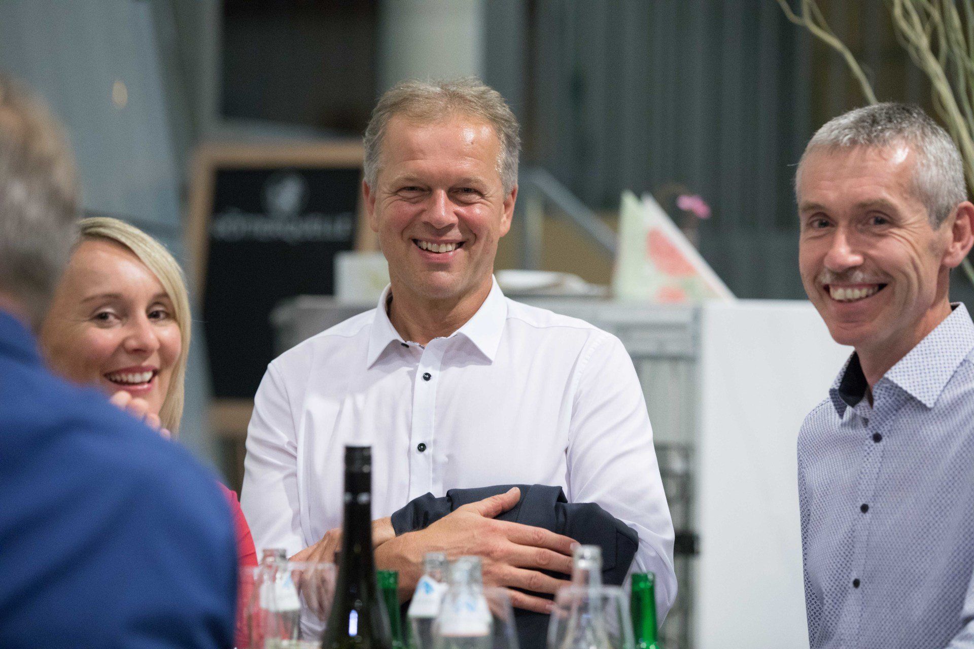 Eine Gruppe von Menschen sitzt mit Weingläsern an einem Tisch und lächelt.