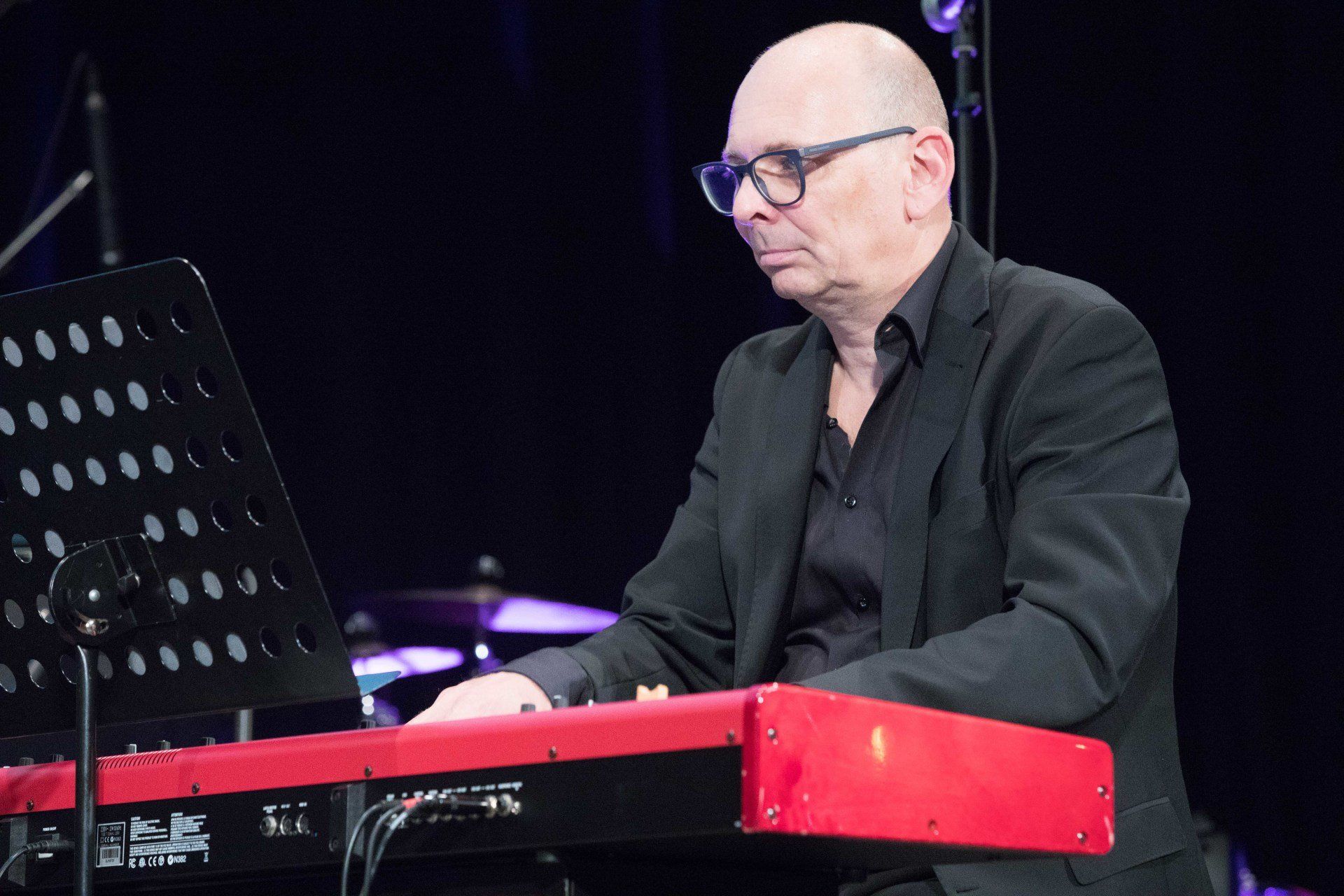 Ein Mann im Anzug spielt auf einer Bühne auf einem roten Keyboard.